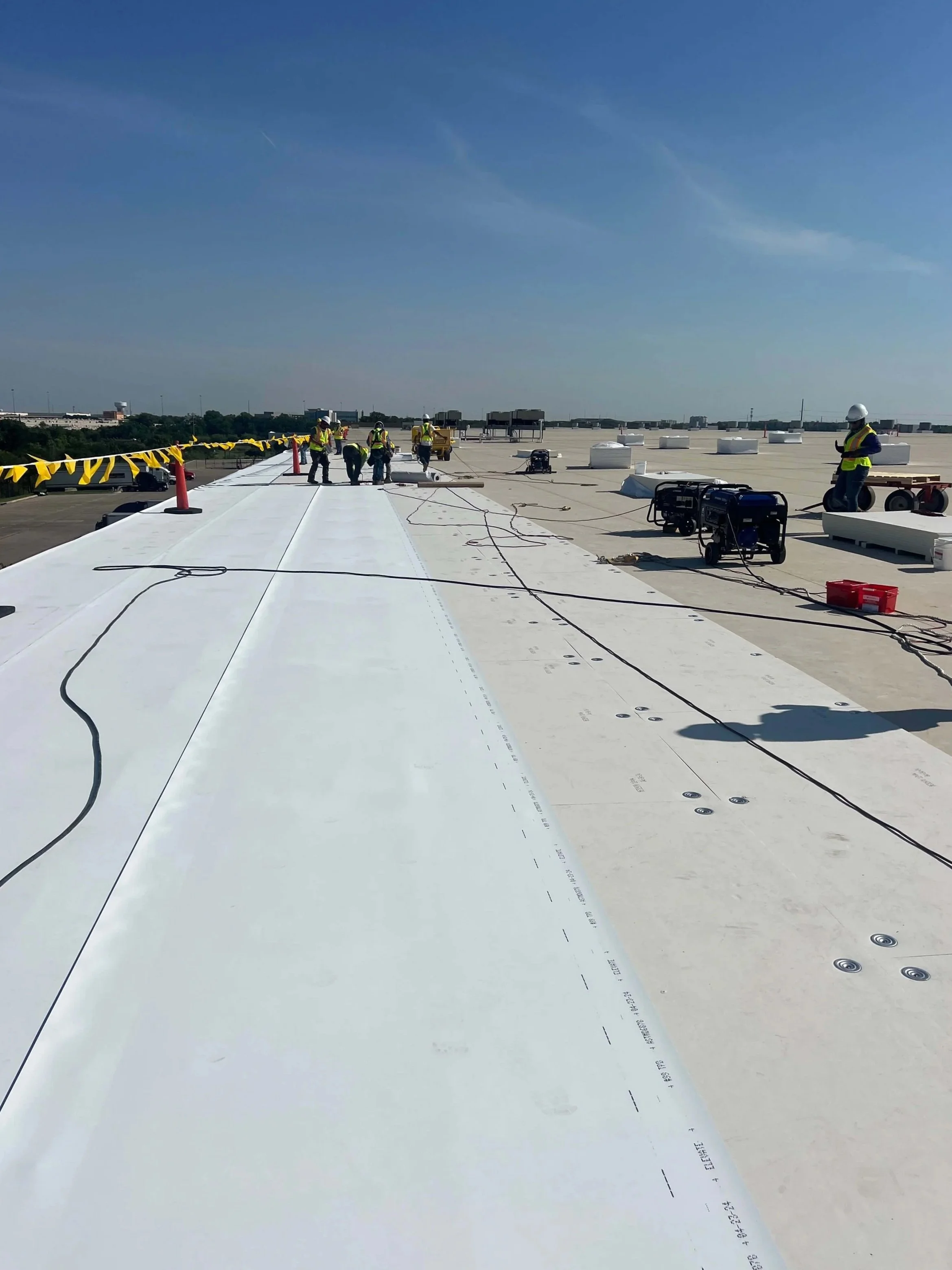 Construction workers installing a white rooftop on a commercial building on a clear, sunny day.
