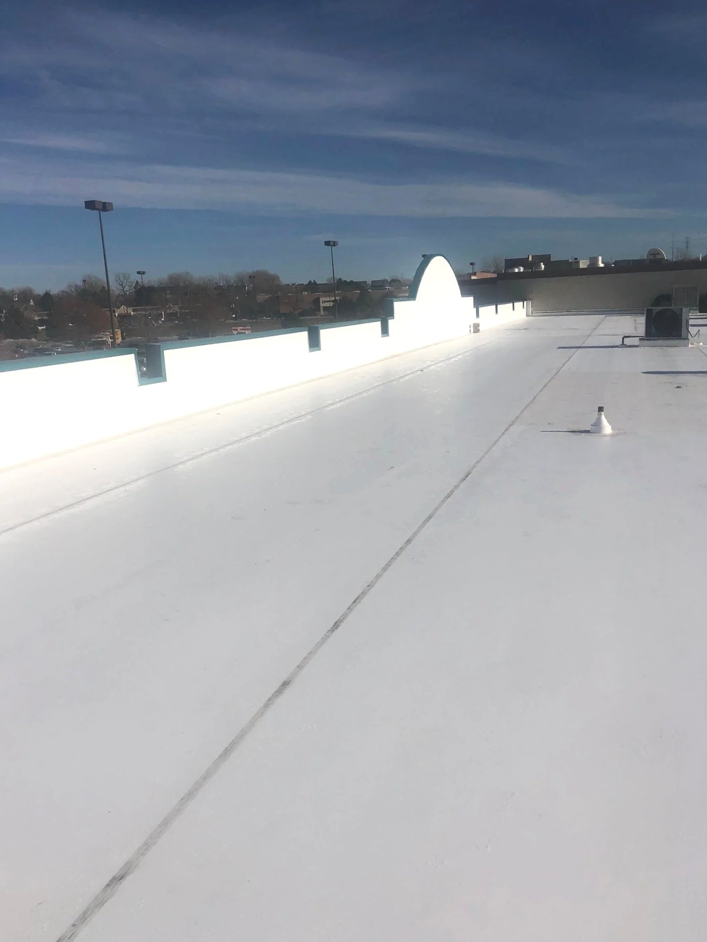 Rooftop with white reflective surface, vents, and lights with a clear blue sky and distant town in the background.