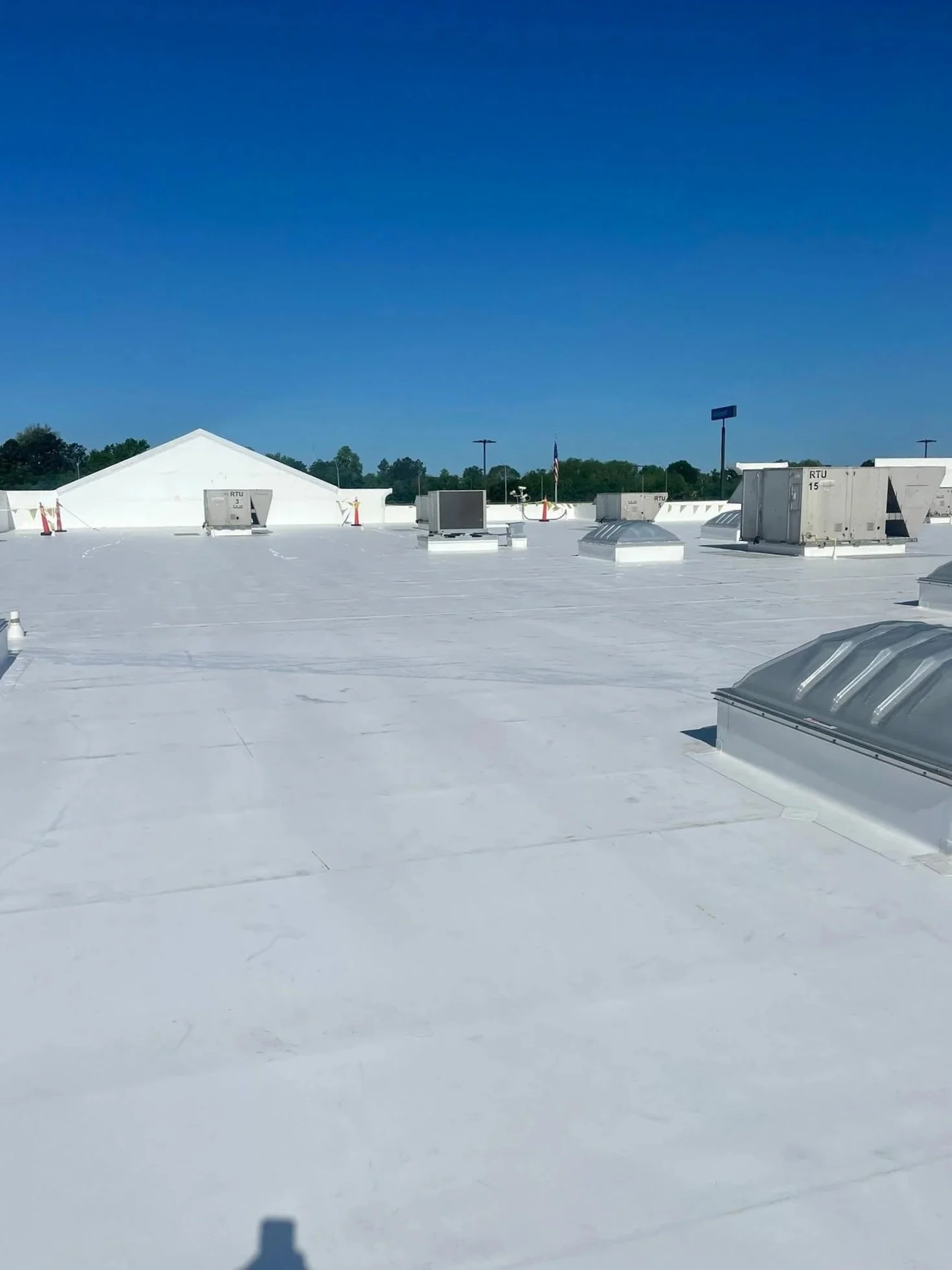 A flat white rooftop with vents and HVAC units, under a clear blue sky, with trees and utility poles in the background.