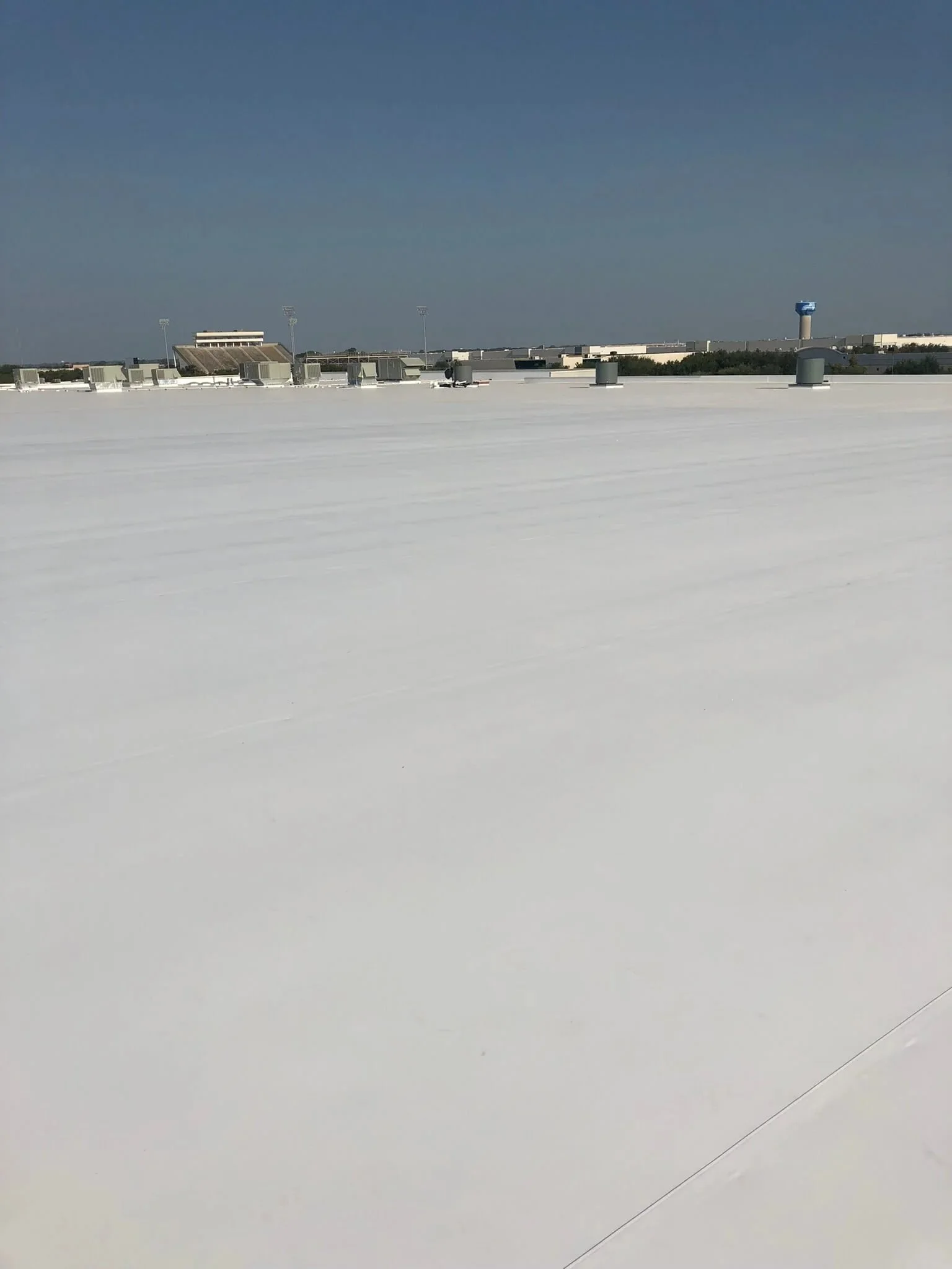 View of the flat, white roof of a large building with HVAC units and vents, under a clear blue sky.