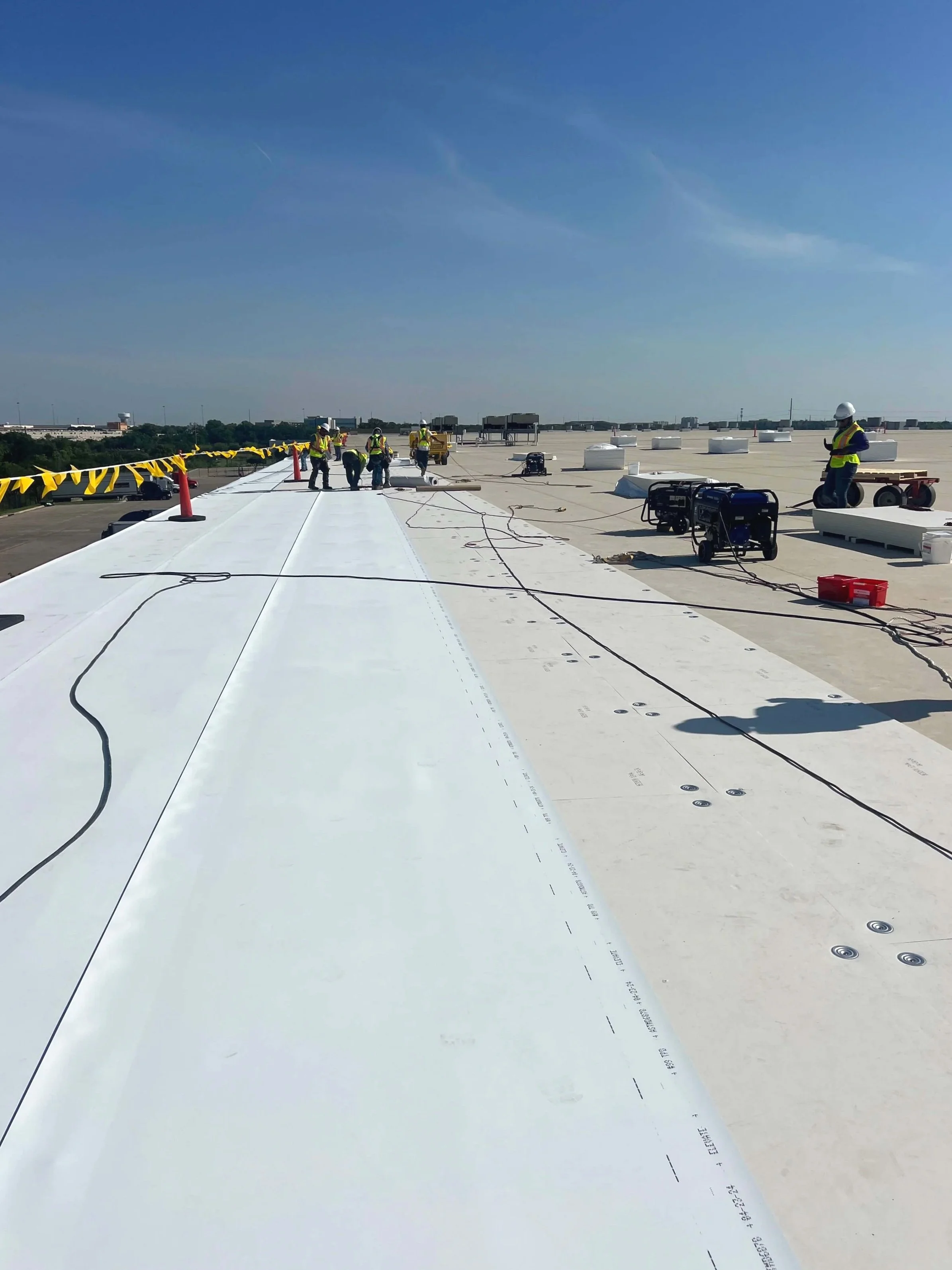 Construction workers installing white roofing panels on a building roof under a clear blue sky.