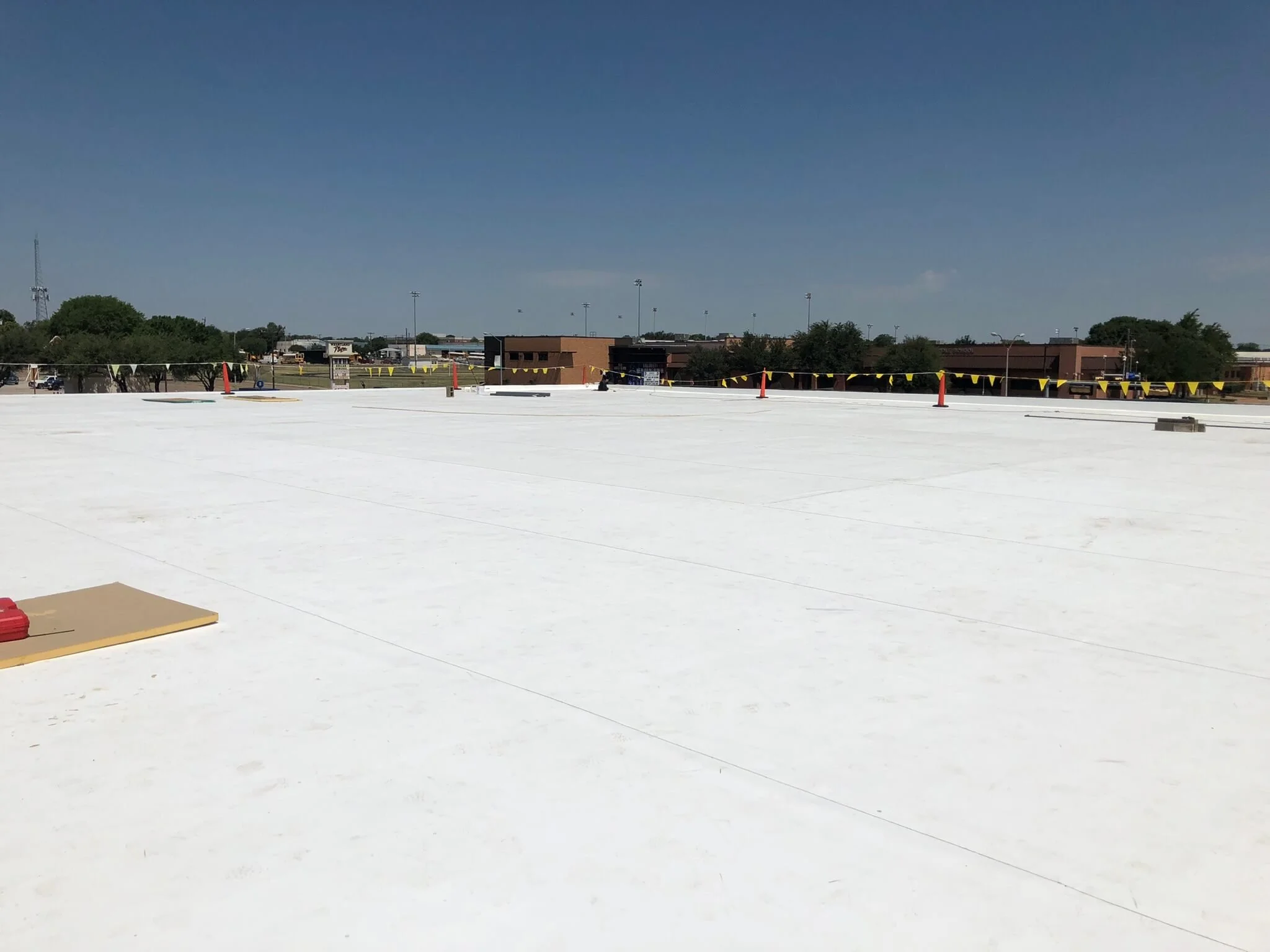 View of a flat white rooftop with a background of trees and buildings under a clear blue sky.