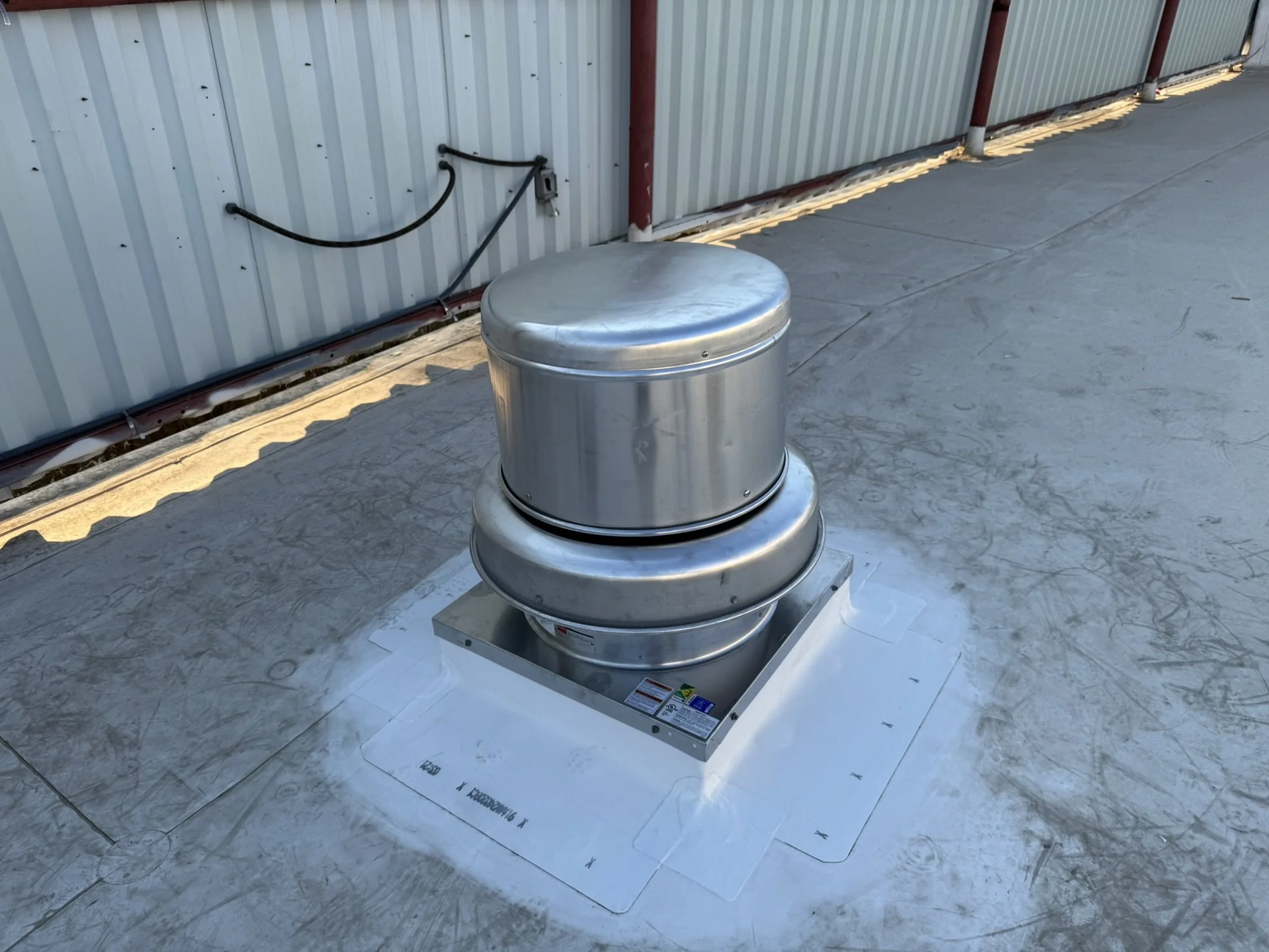 A metal roof vent on a flat rooftop next to a corrugated metal building wall.