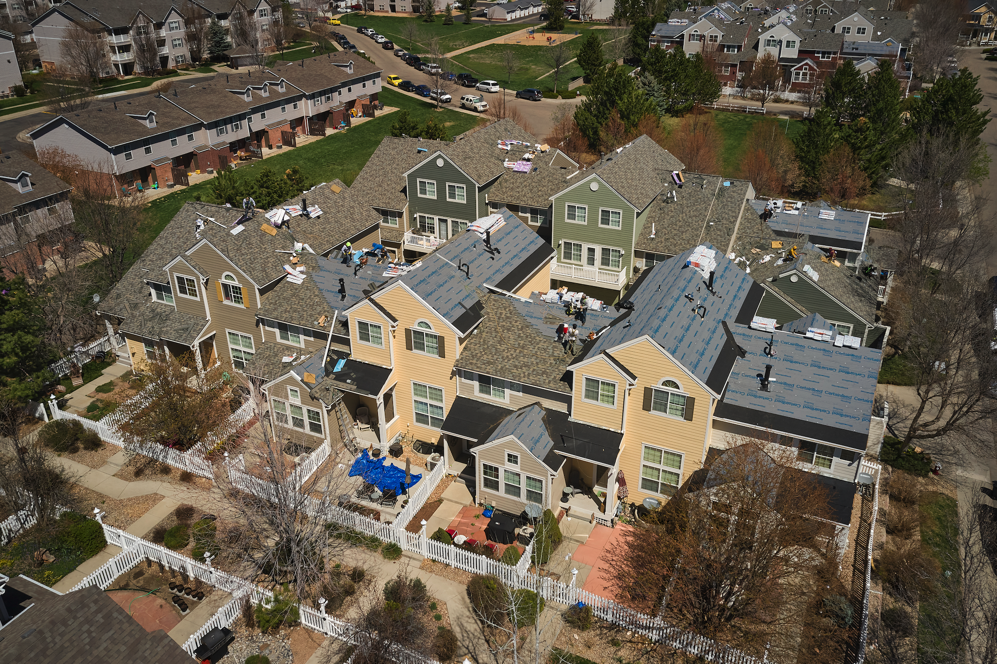 Aerial view of a residential neighborhood in Colorado with multiple two-story houses under construction, some roofs partially completed, and workers on the roofs.