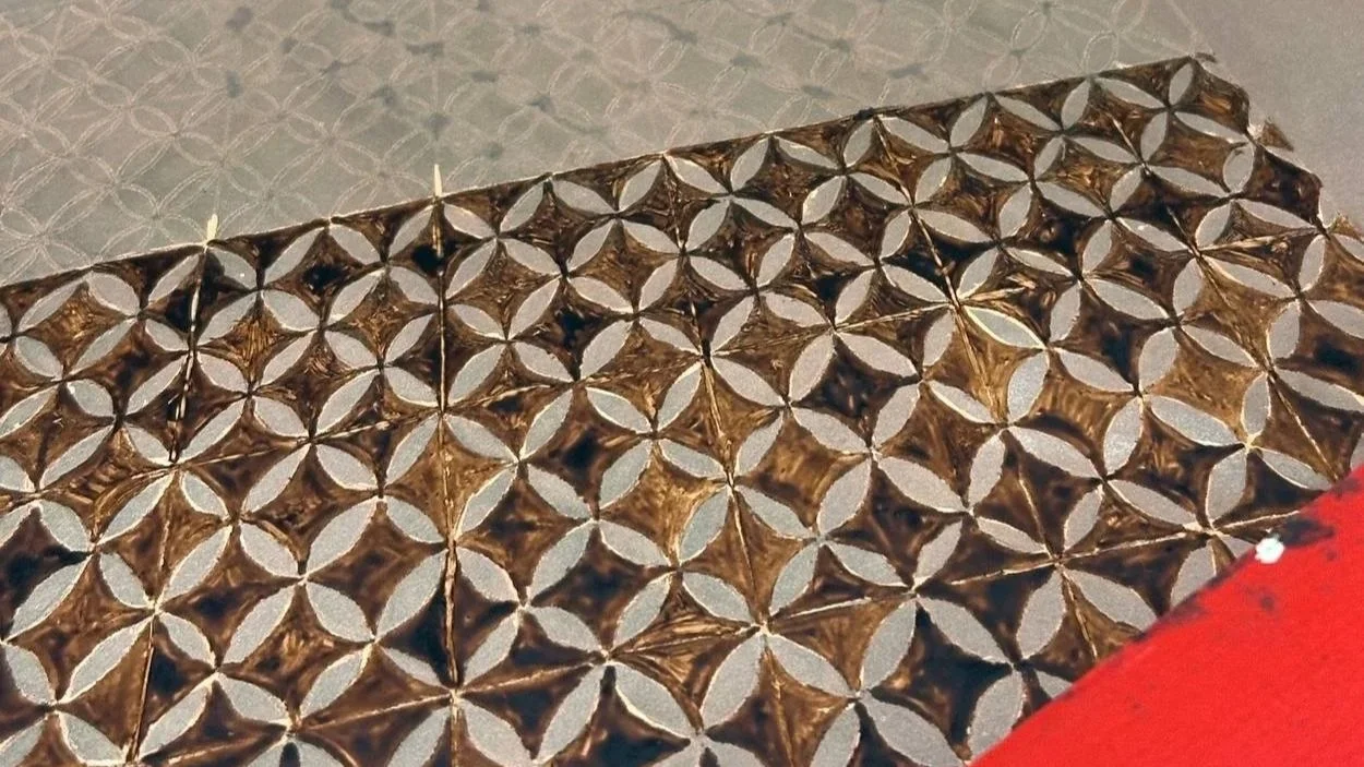 Patrón decorativo dorado con forma de estrellas en un fondo gris, parcialmente cubierto por una esquina roja.