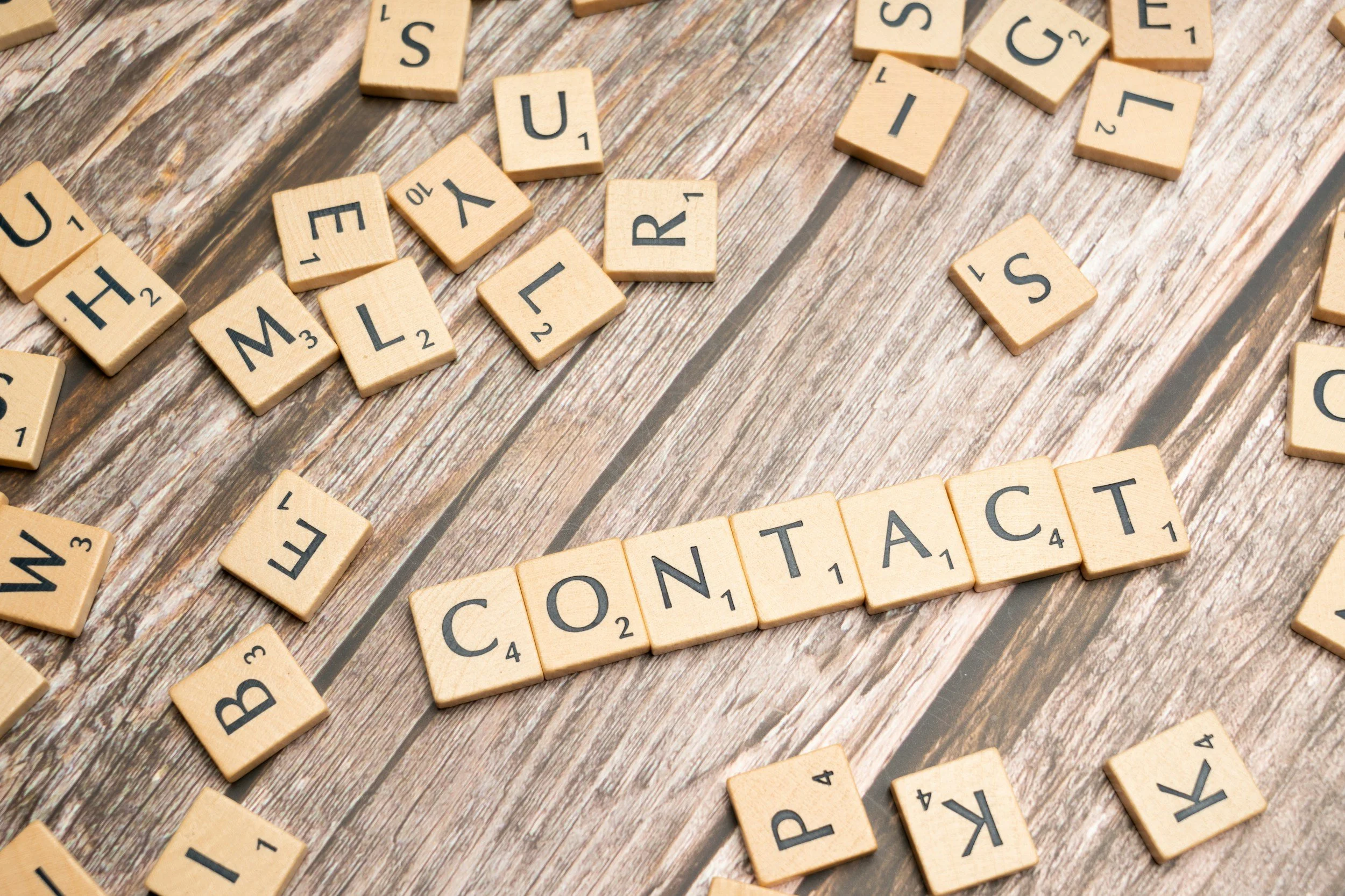 Scrabble tiles spelling 'CONTACT' on a wooden surface, surrounded by scattered individual letter tiles.  A reminder to contact Watermark ADI with your questions.  This is how you get in touch with us.