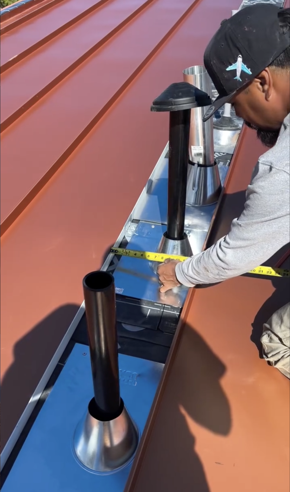 A person measuring a metal vent on a new copper roof with a tape measure, with several similar vents and roof panels visible in San Jose, CA.
