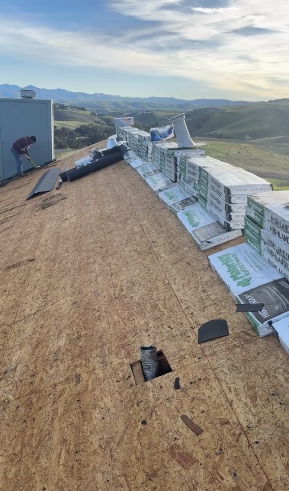 A rooftop with building materials, including stacks of insulation and roofing paper, with a worker on the left installing or inspecting the roofing in Morgan Hill CA.