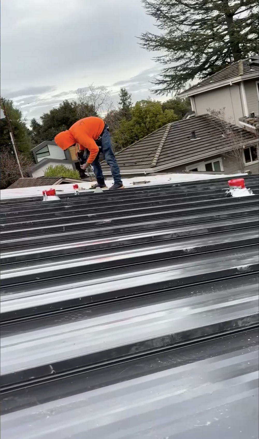 A worker in an orange hoodie installing or repairing a metal roof on a residential building in Morgan Hill, CA.
