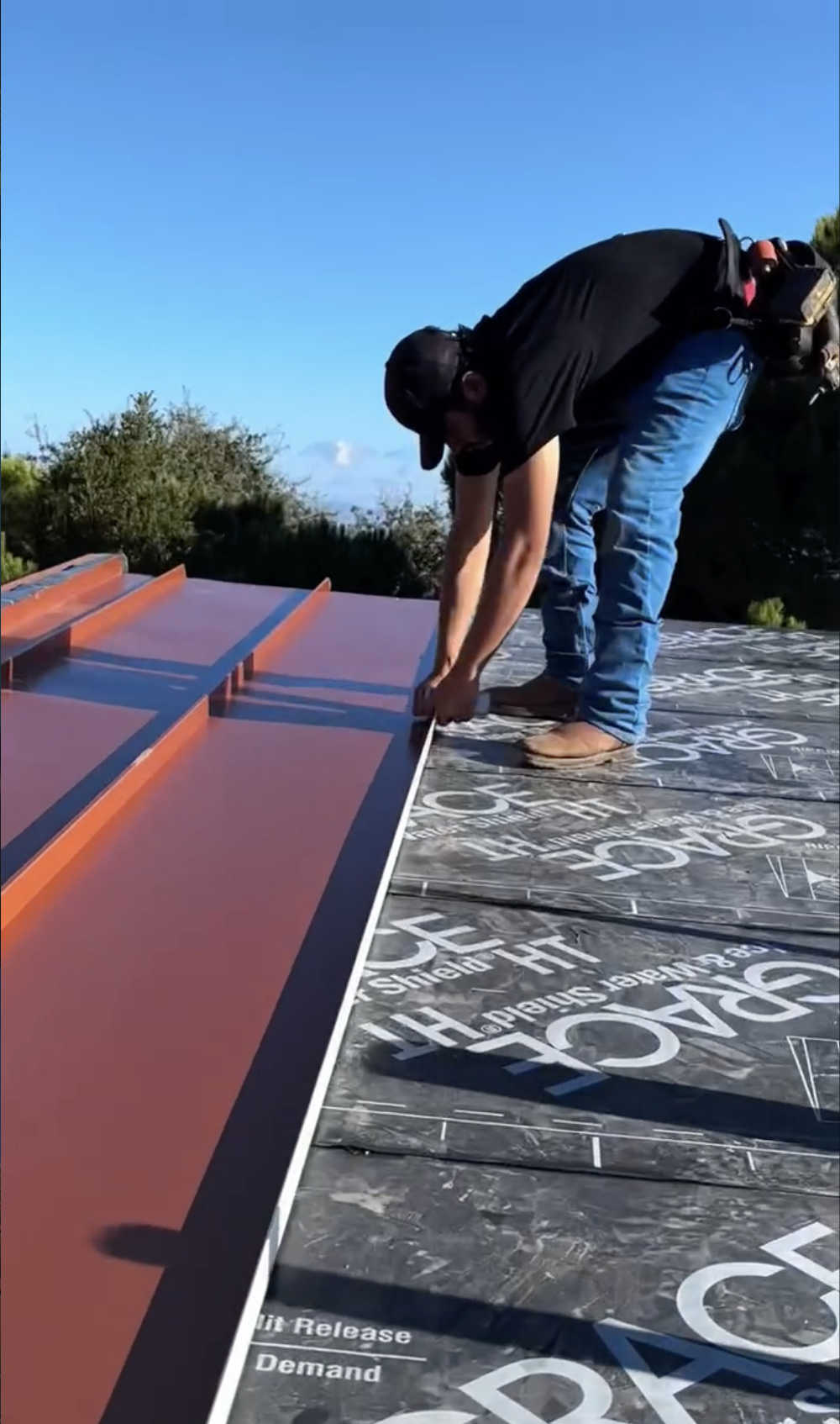 A person working on a copper sheet metal roof of a modern, multi-story building with black siding, large windows in San Jose, CA. 