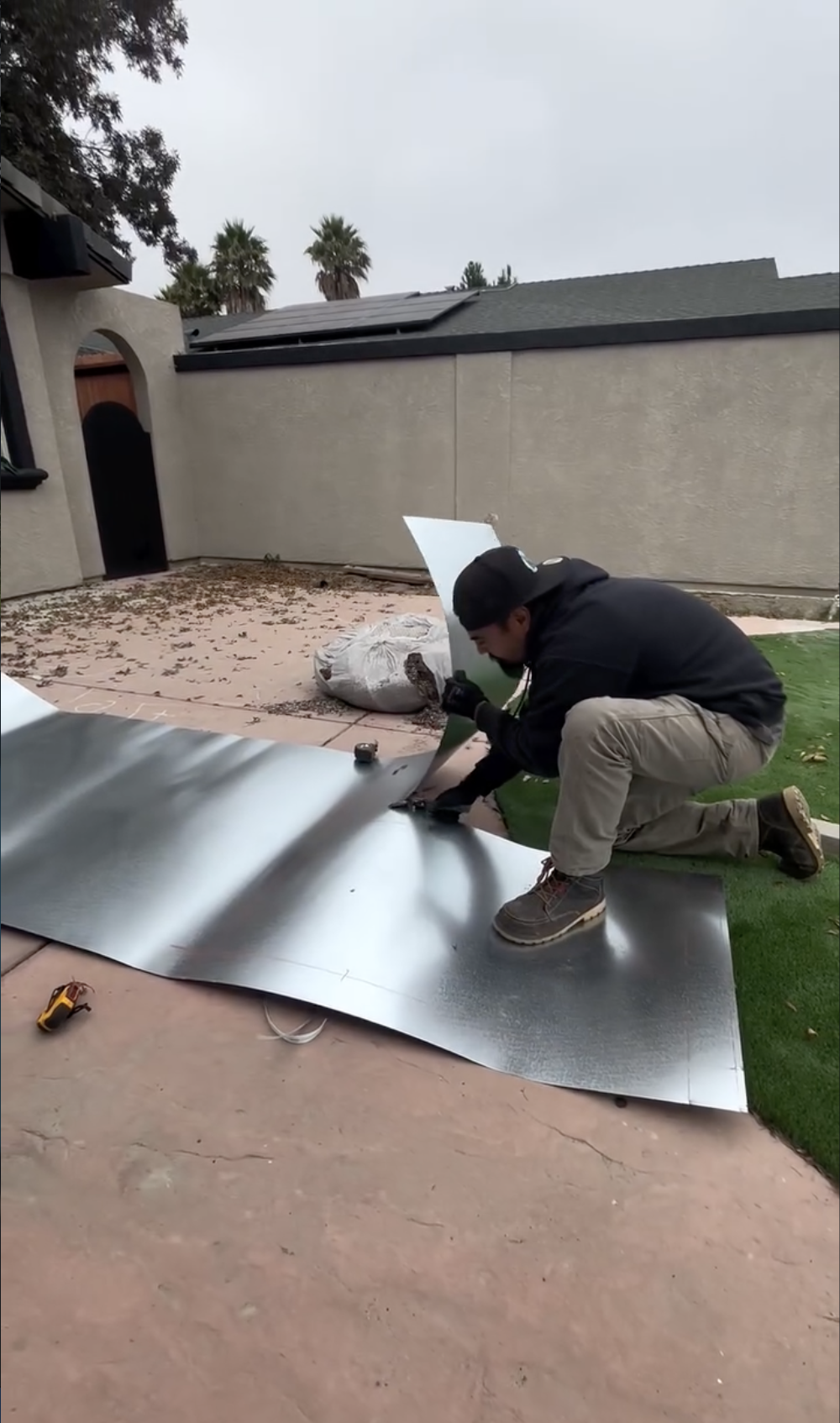 A man kneeling on PB Garden Artificial Grass while working on a large sheet metal project in Hollister, CA.