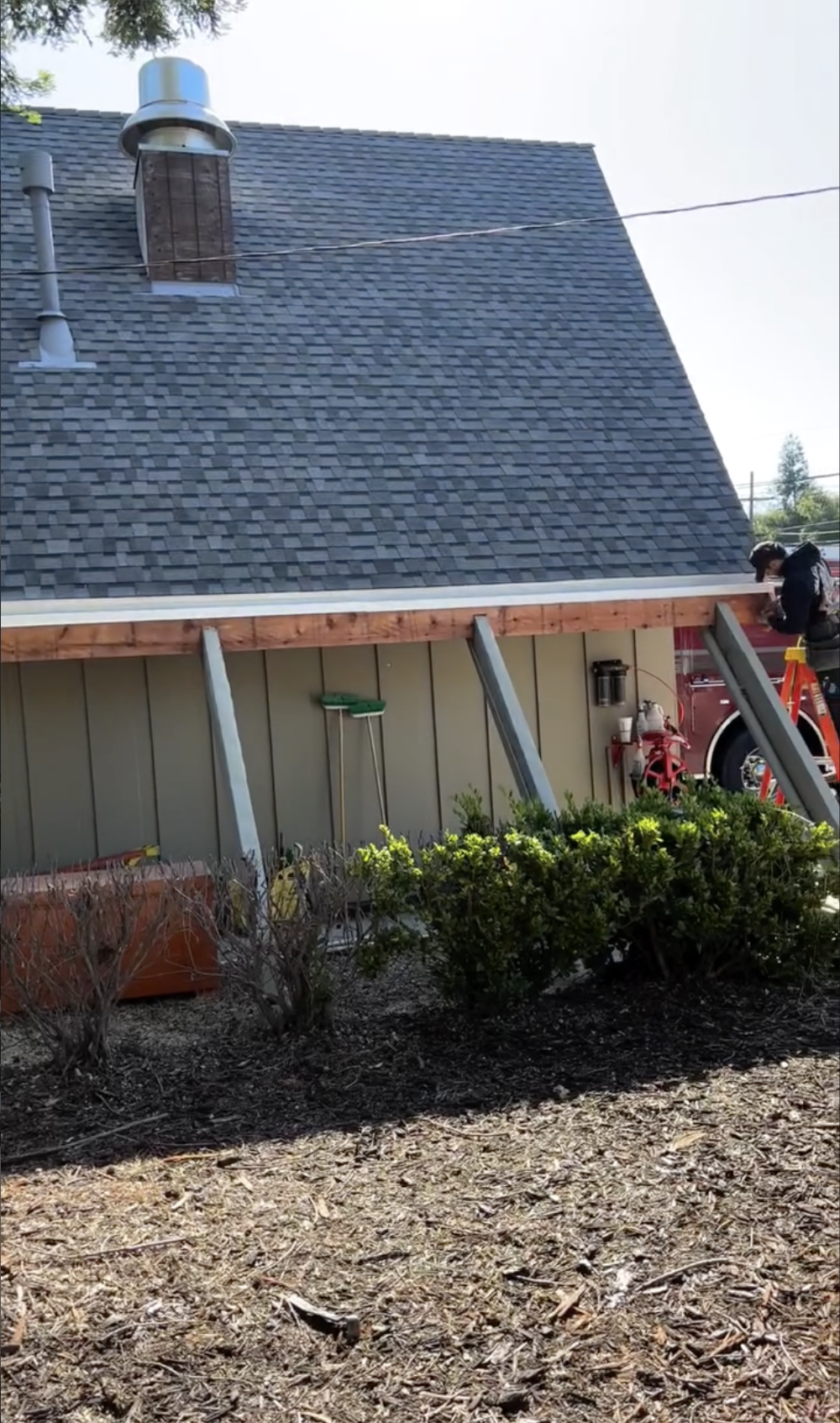 Construction worker on a ladder working on the roof of a house with a steep roof, chimney, and a red fire truck nearby in San Benito County. 