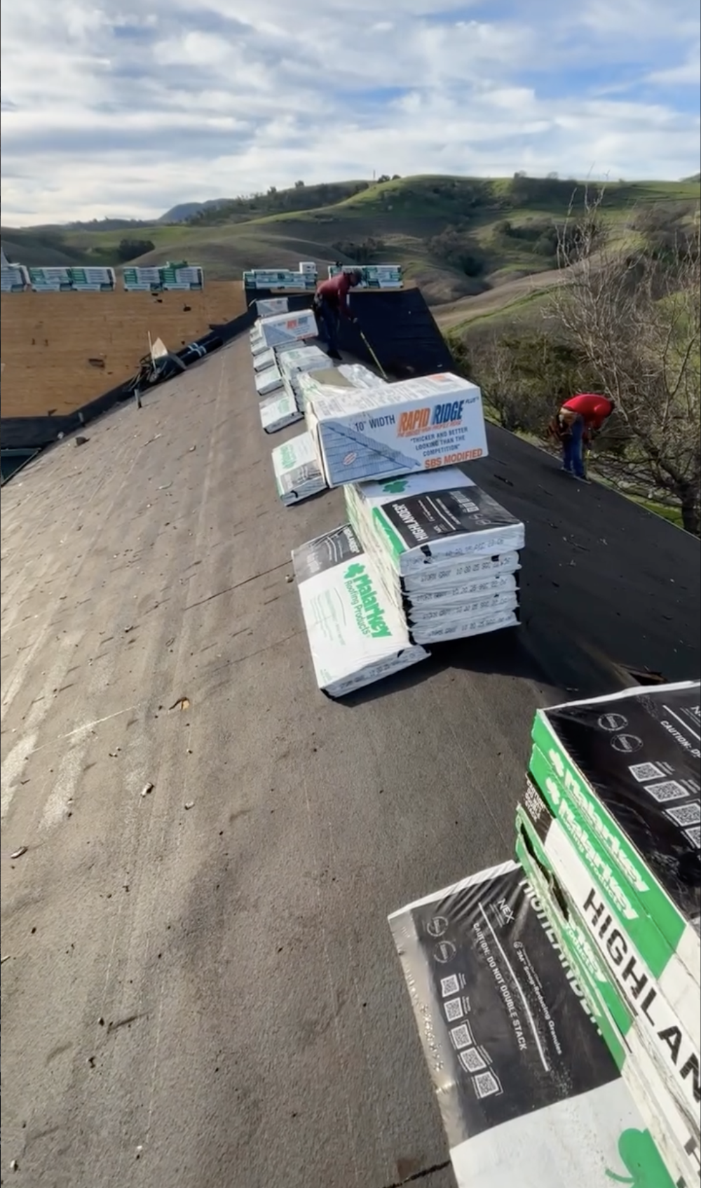 Two workers installing roofing insulation sheets on a rooftop with a scenic countryside and hills in the background In Morgan Hill, CA.
