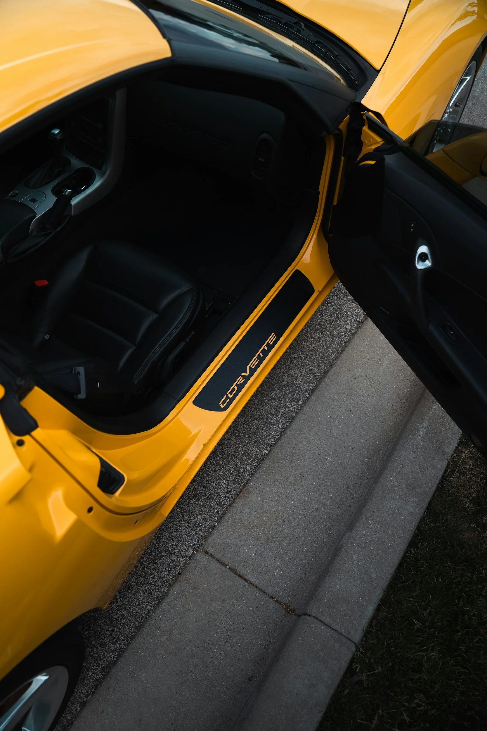 Top-down view of a yellow C6 Corvette parked with its door open, revealing the black interior and dashboard.