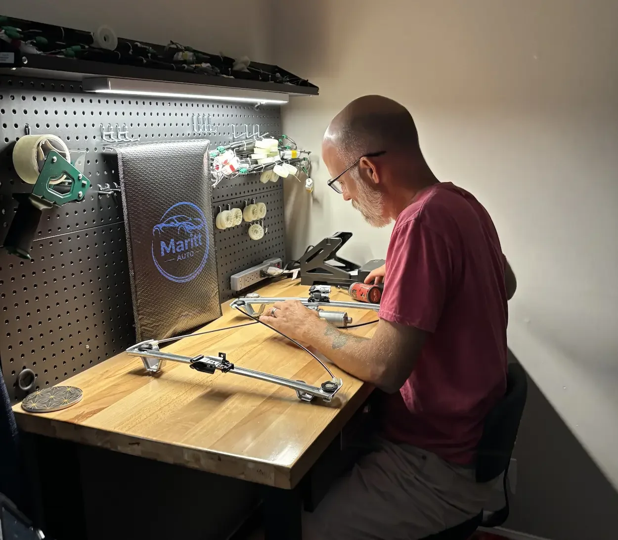 Man working on automotive parts at a wooden workbench with tools and equipment in a garage or workshop.