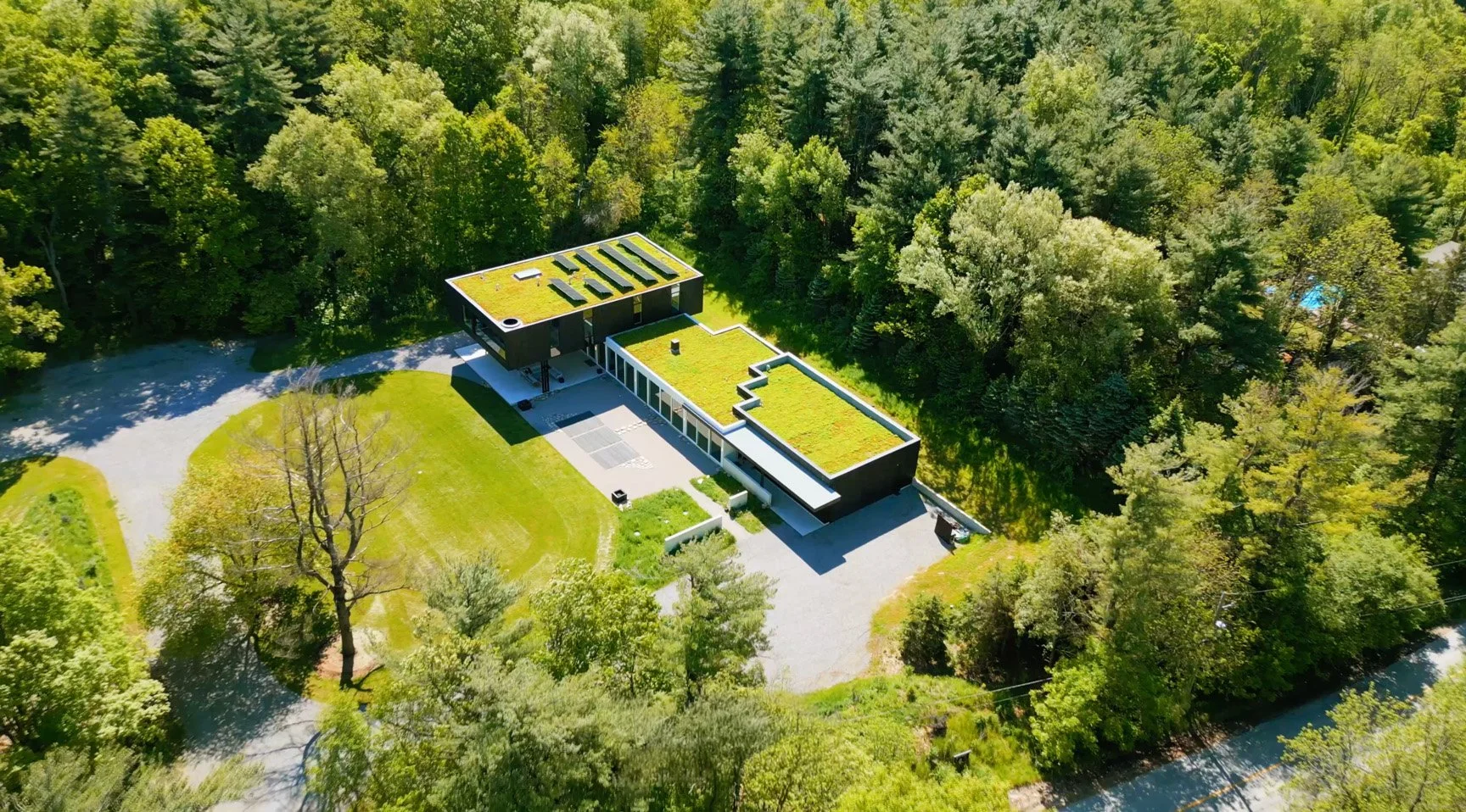 Aerial view of a modern house with a green roof surrounded by tall trees and a driveway.