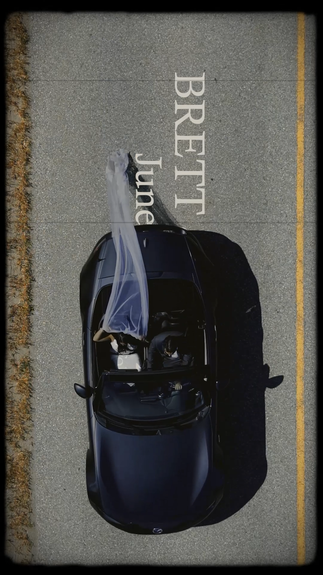 Top-down view of a black car with a driver sitting inside, parked on a road with a snow-white plastic sheet draped over part of the vehicle. The road has yellow lines and text that reads 'BRETLIJ blue line'.