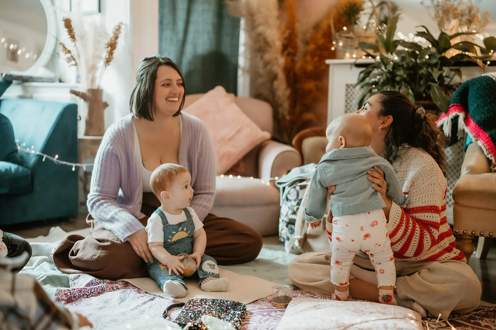 Two women and two young children sitting on the floor in a cozy living room decorated for Christmas.