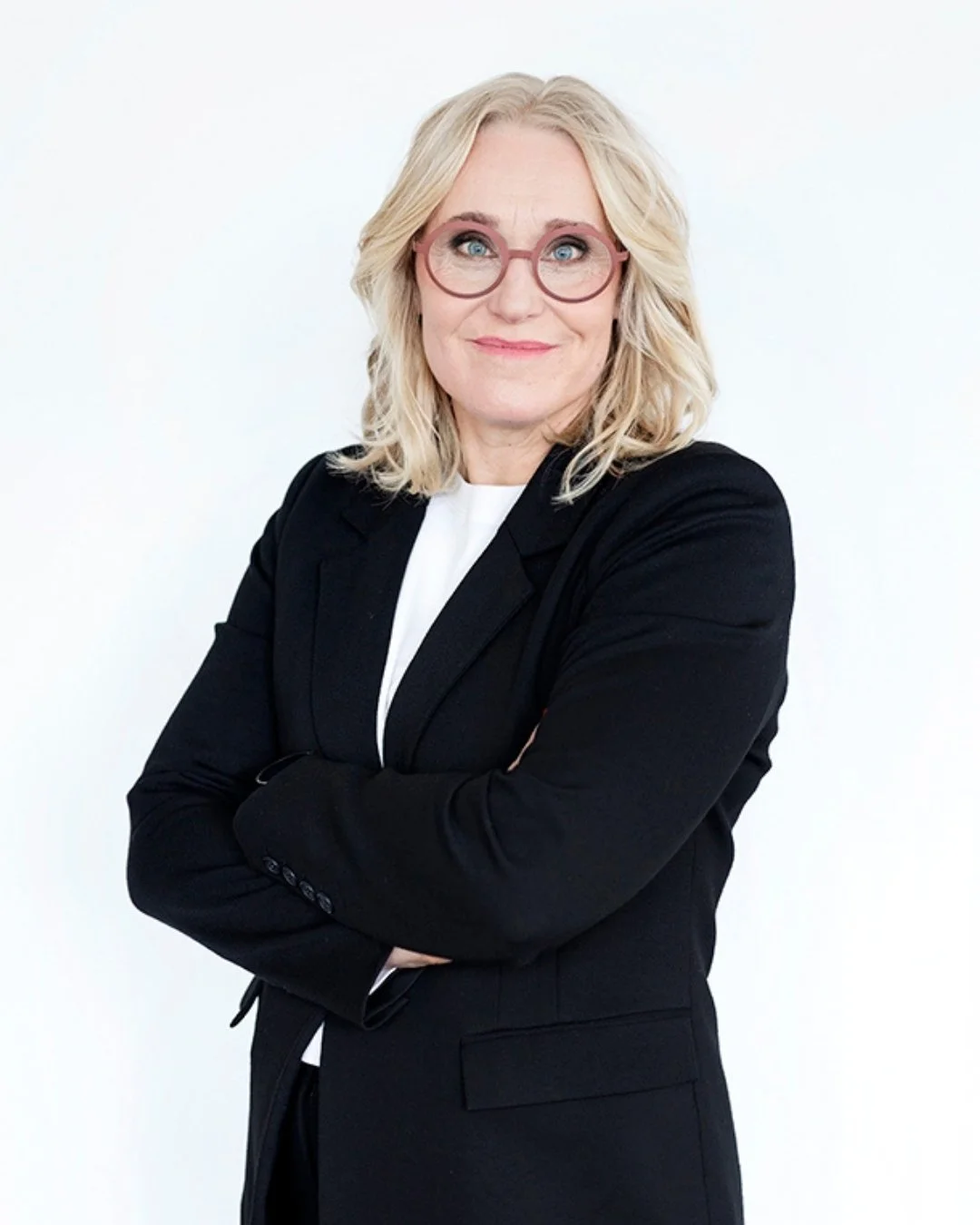 Johanna seisoo kädet ristissä mustassa bleiserissä ja hymyilee kameralle.