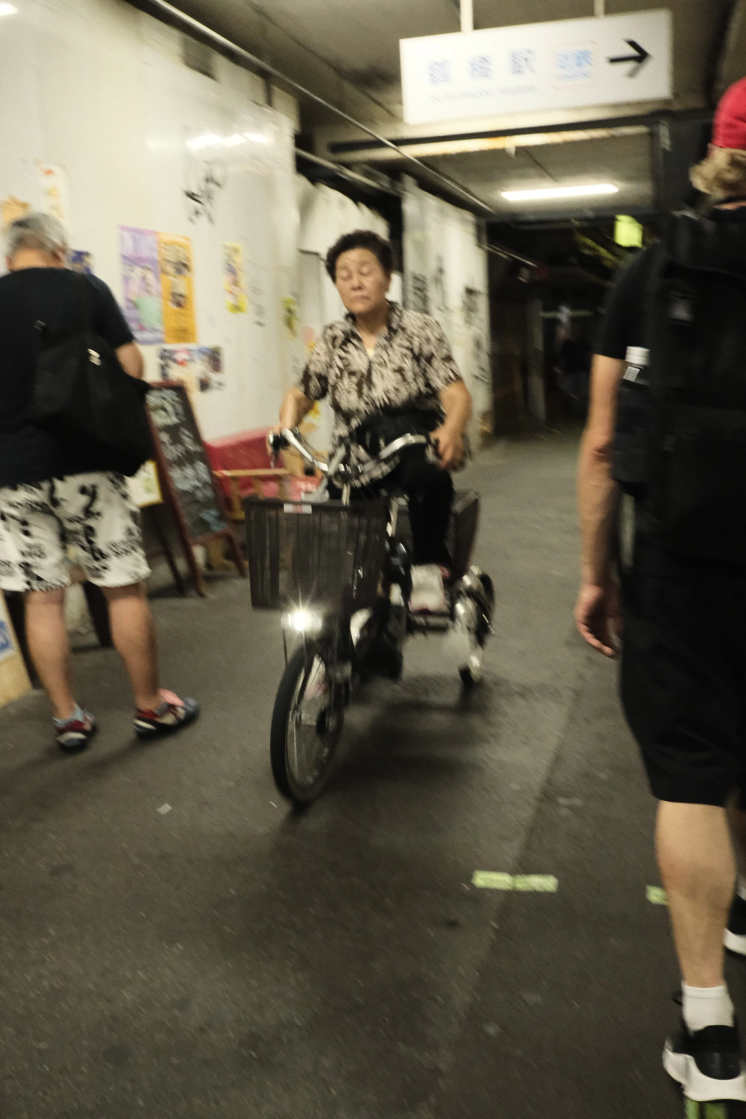 A woman wearing a patterned shirt riding a bike through an underground parking garage with other people around.