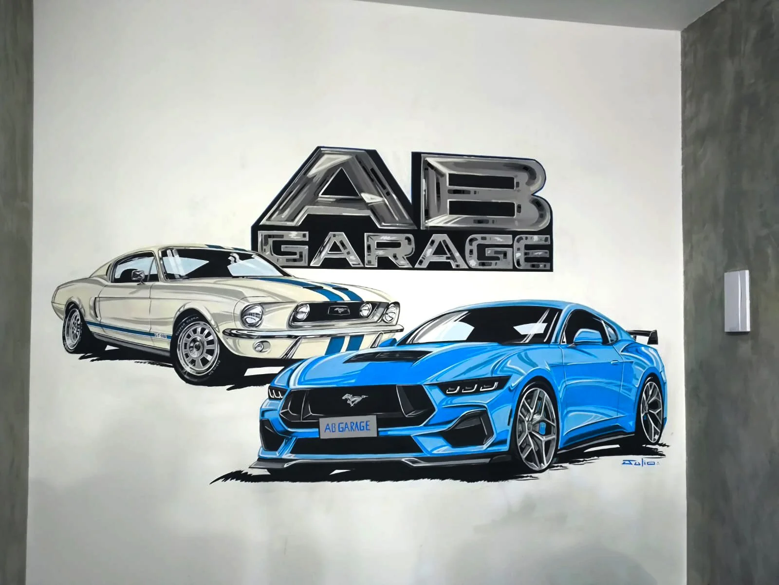 Hand-painted automotive wall mural by JCARCUSTOM featuring a classic white Ford Mustang with blue stripes, a modern blue Ford Mustang, and the AB Garage logo in São Paulo, Brazil.  Copiar