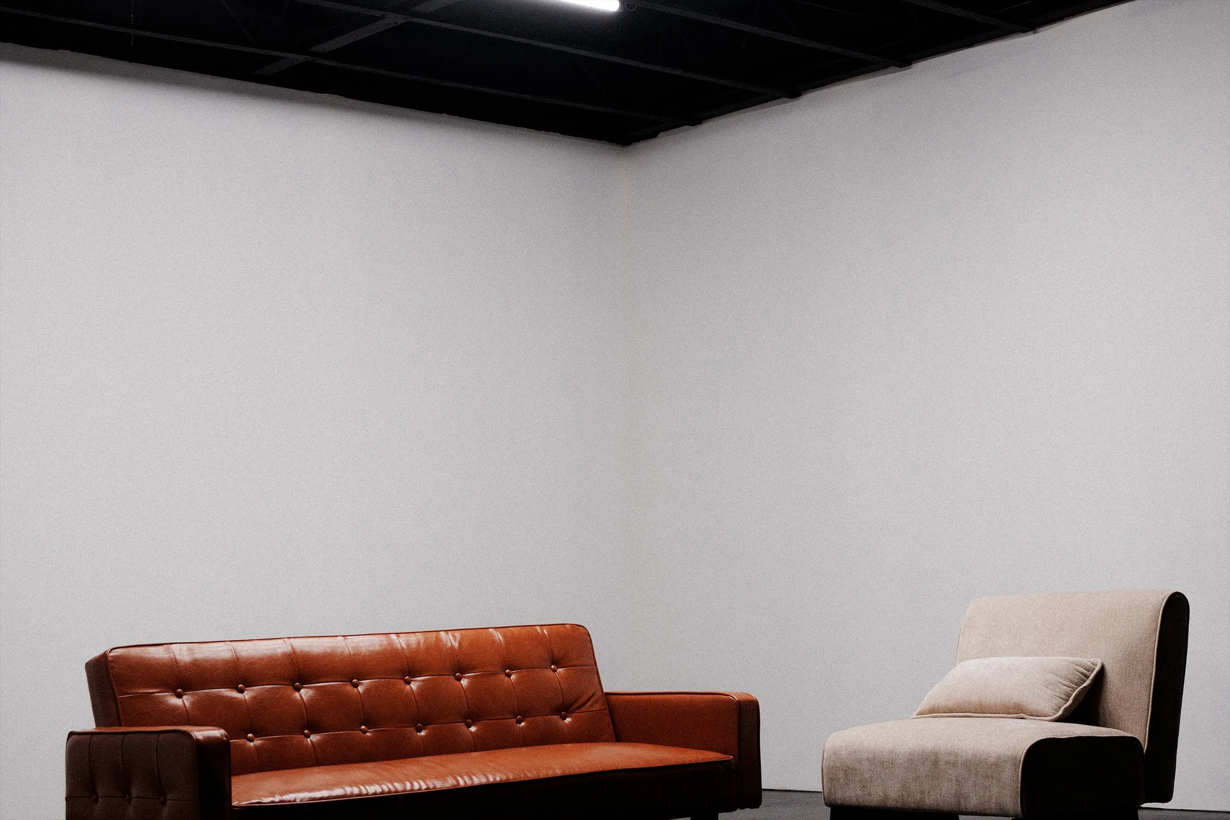 Interior of a modern room with a dark ceiling, white walls, a brown leather tufted sofa, and a cream-colored armchair.