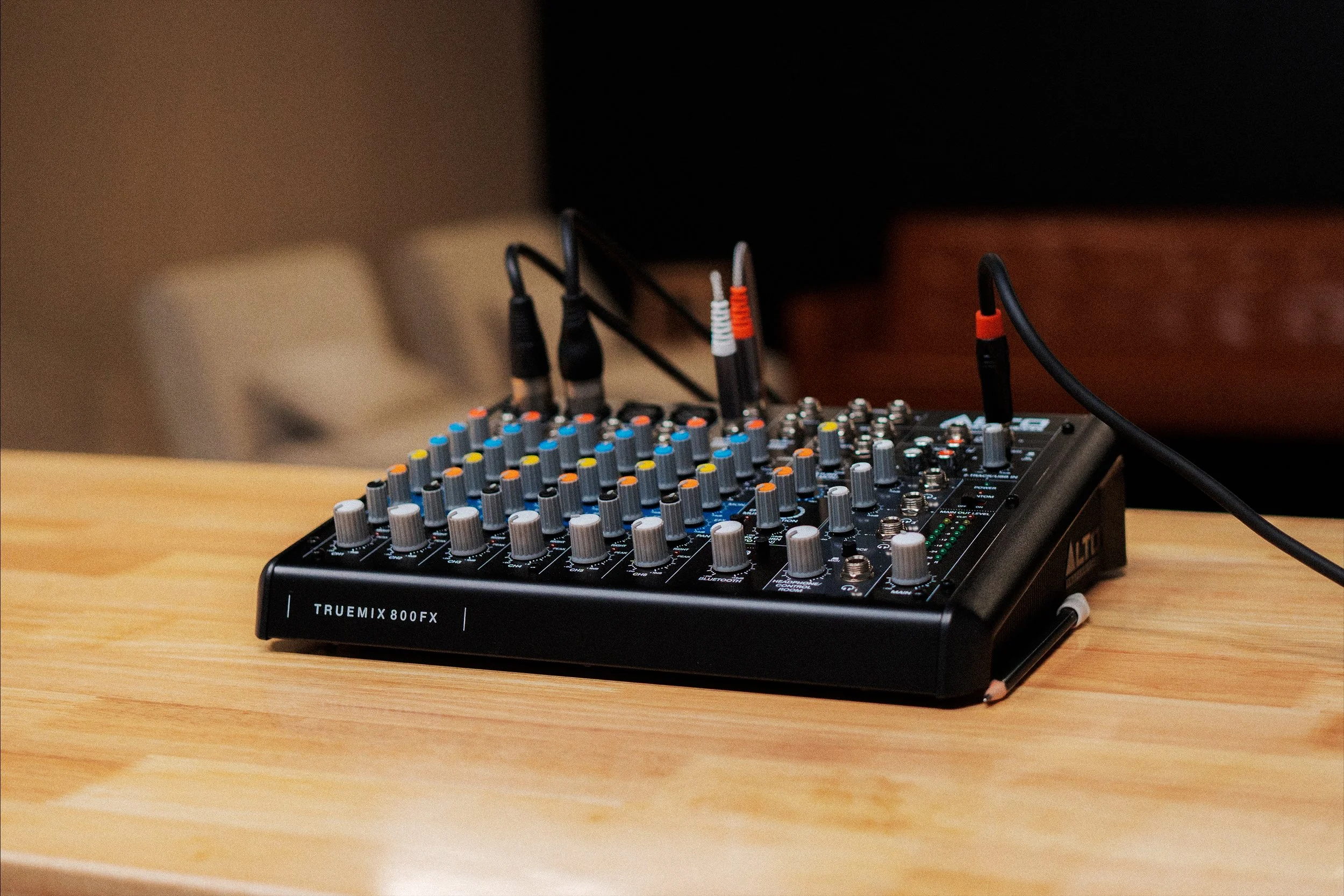 A black audio mixer with multiple colorful control knobs and cables connected, placed on a wooden table.