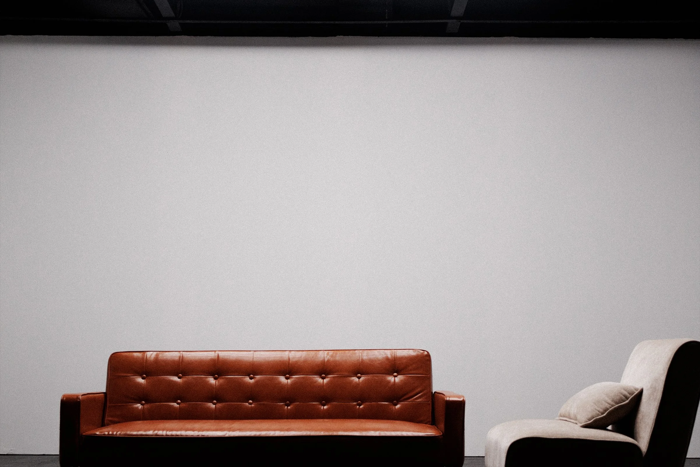A brown leather sofa and a beige upholstered armchair with a pillow in a room with a gray wall.