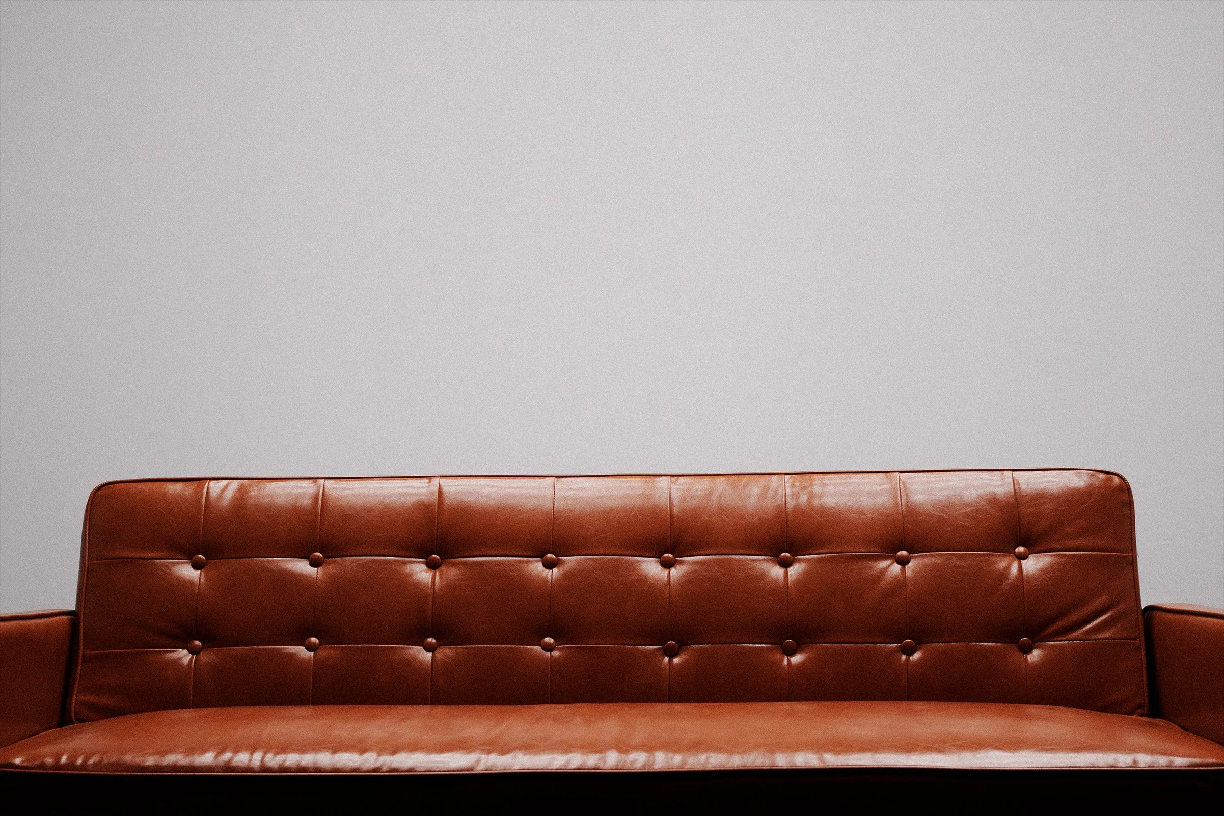 A brown leather sofa with button tufting against a plain light gray wall.