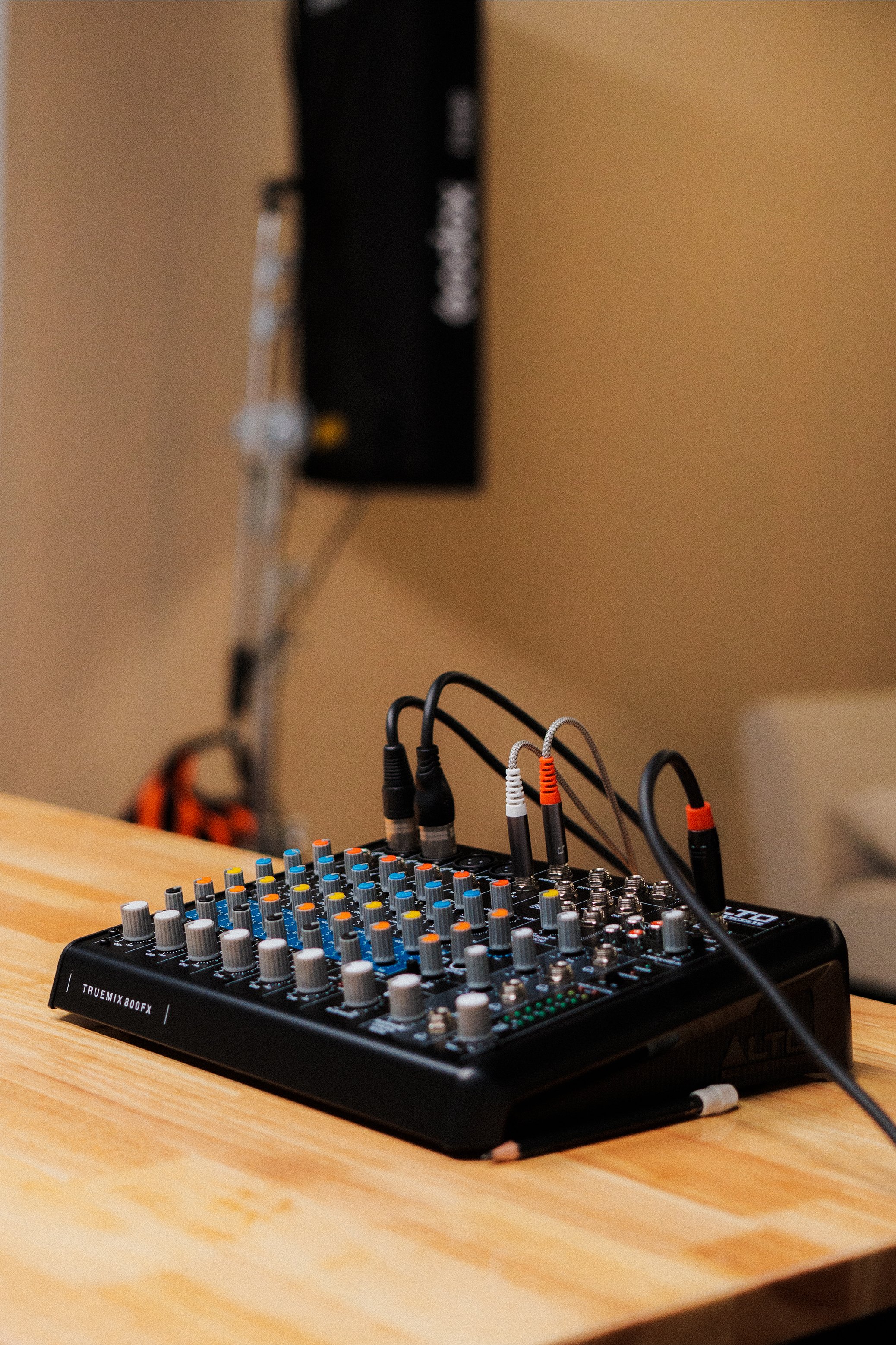 A sound mixing console on a wooden table with various colored knobs and several connected cables.