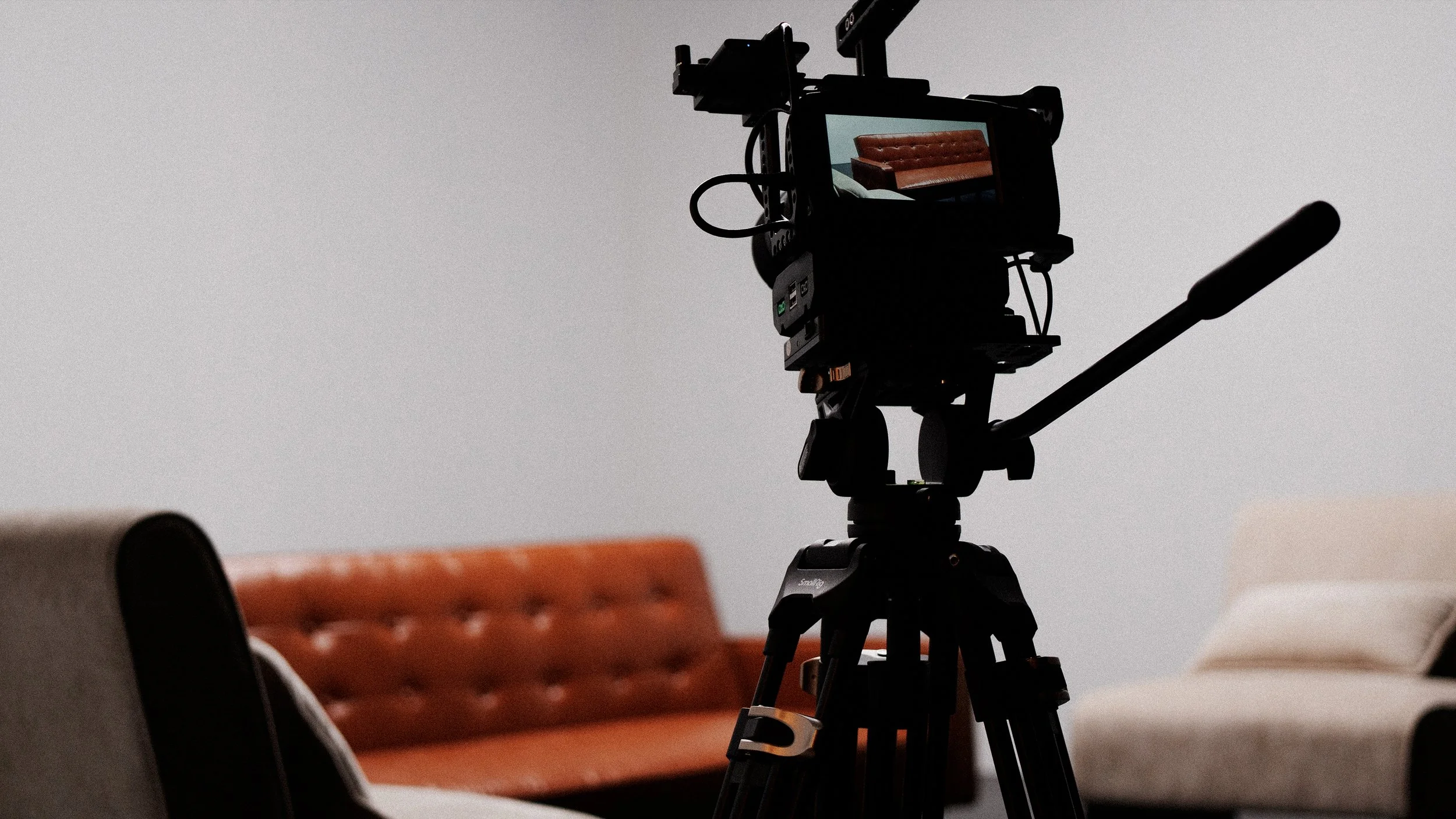 A camera on a tripod positioned in front of an orange lounge chair, with another piece of furniture blurred in the foreground.
