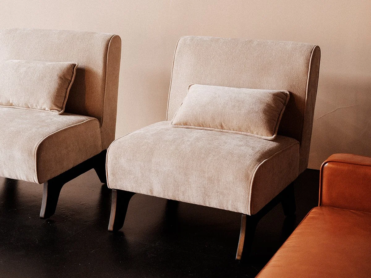 Two beige armchairs with pillows and dark wooden legs, one partly visible on the right.