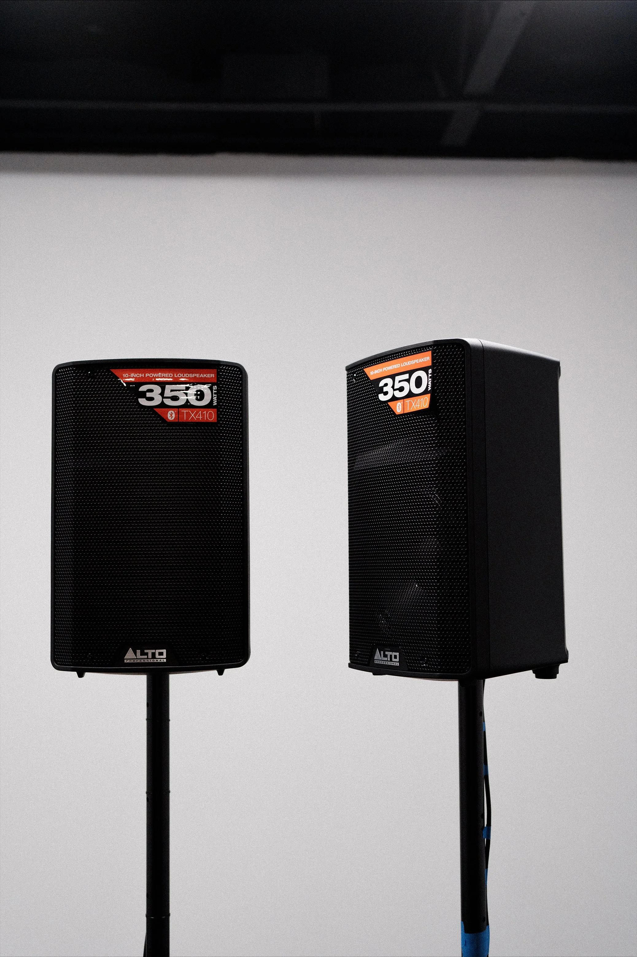 Two black Alto professional speakers on stands against a plain light gray background.