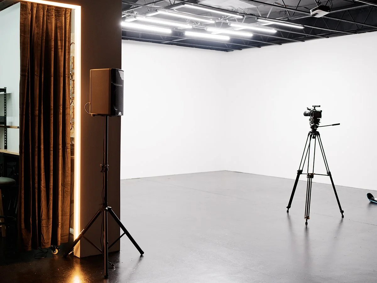 Empty photography studio with camera on tripod, studio light, white wall, and brown curtain