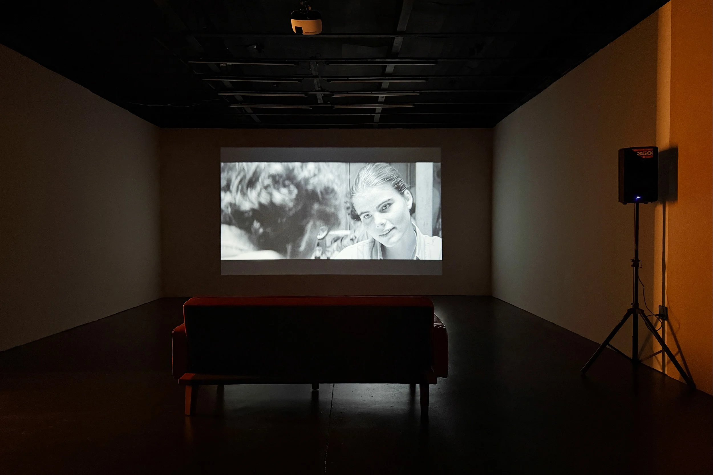 A black-and-white movie scene projected on a wall, showcasing a close-up of a young woman with a serious expression.