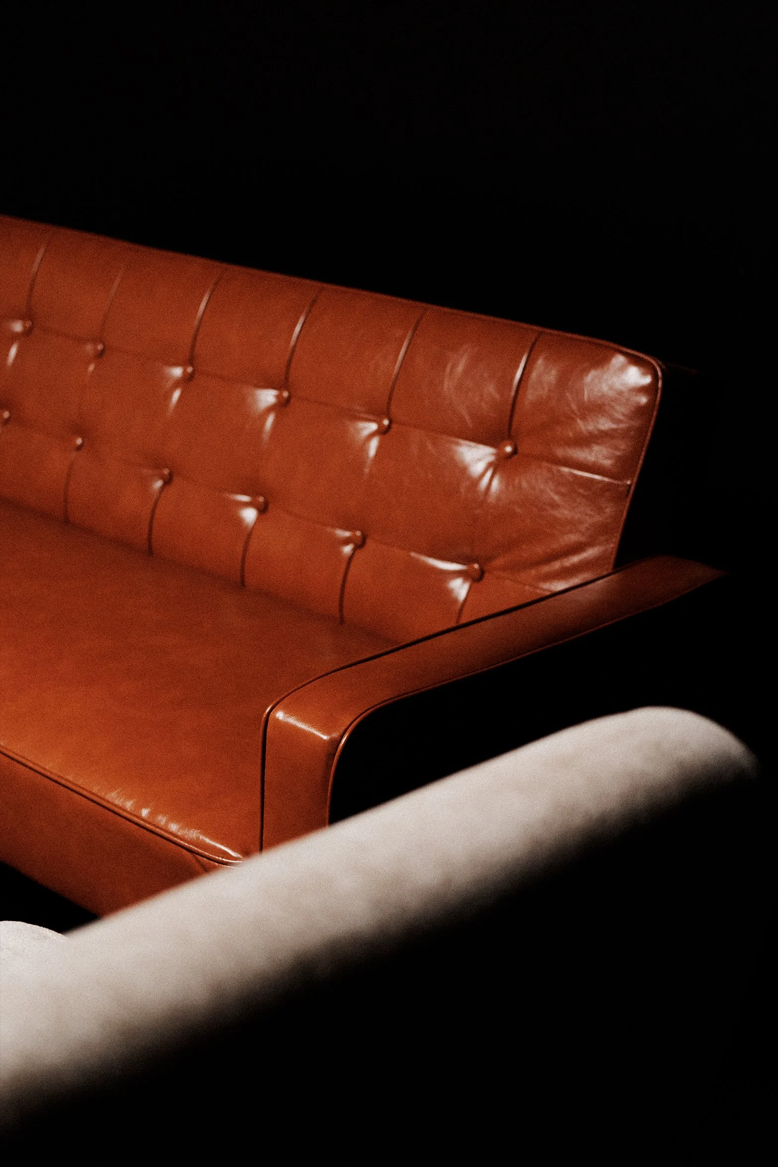 Close-up of a vintage brown leather tufted sofa against a black background.