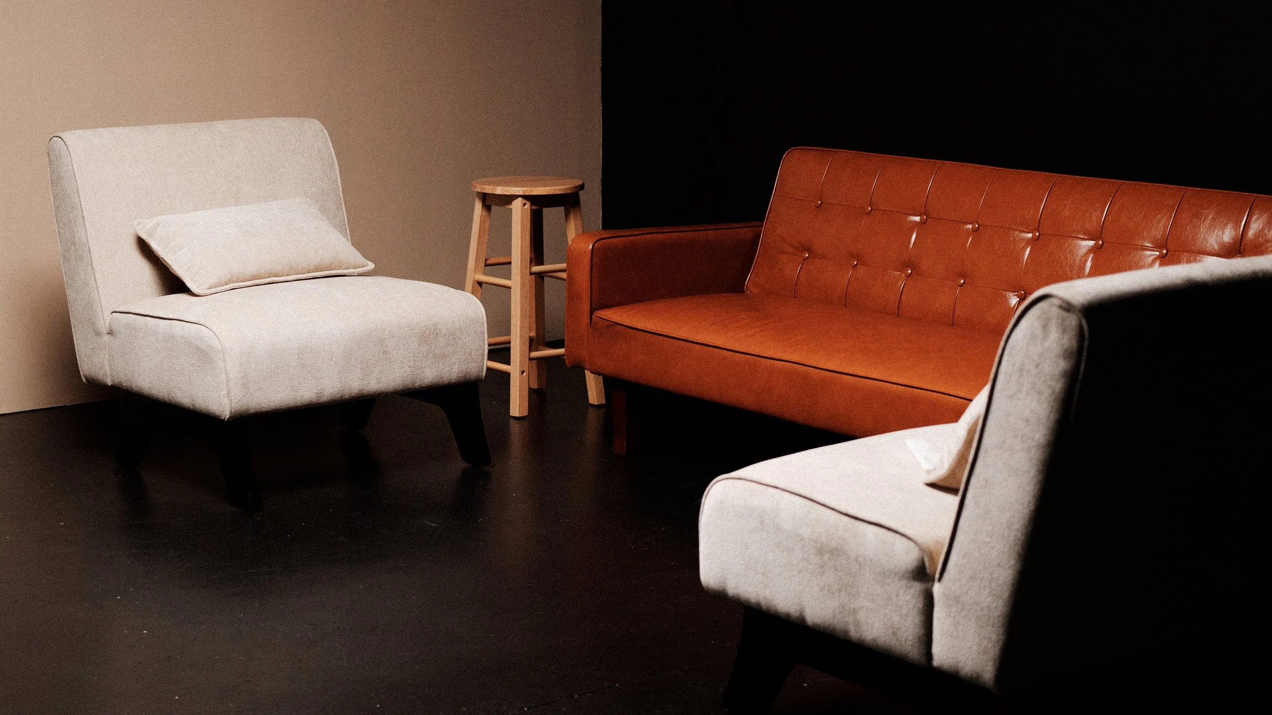 A cozy seating area with a beige armchair, a burnt orange leather sofa, a small wooden side table, and a black and beige wall background.