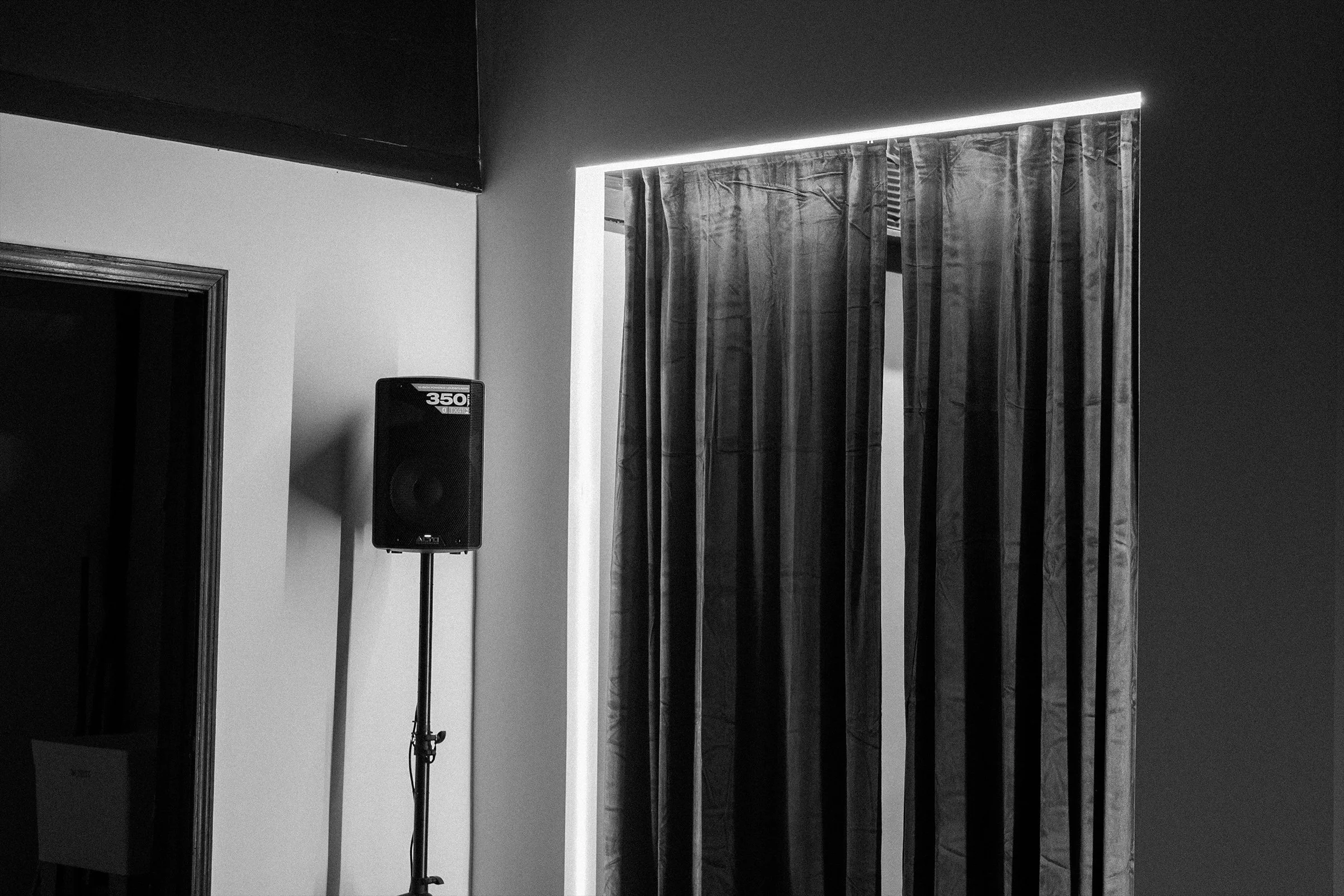 Interior room with a window covered by curtains, and a speaker on a stand, visible in a black and white photo.