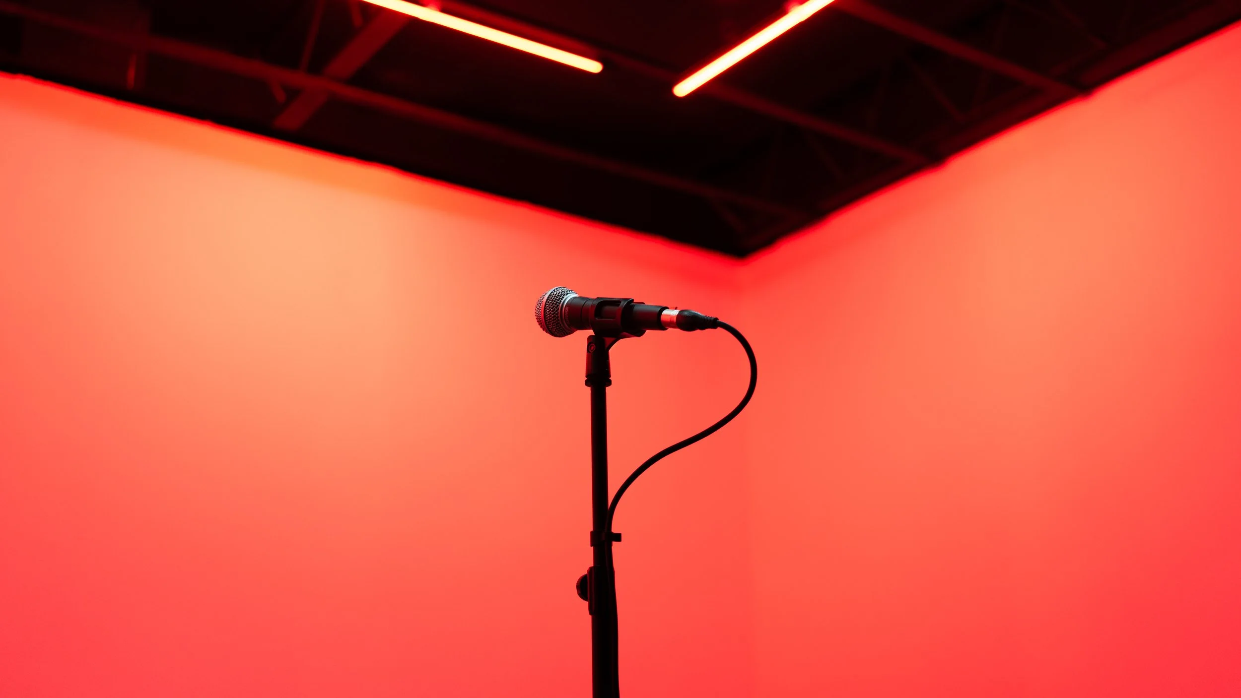 A microphone on a stand in front of a red background with a ceiling featuring red lighting strips.