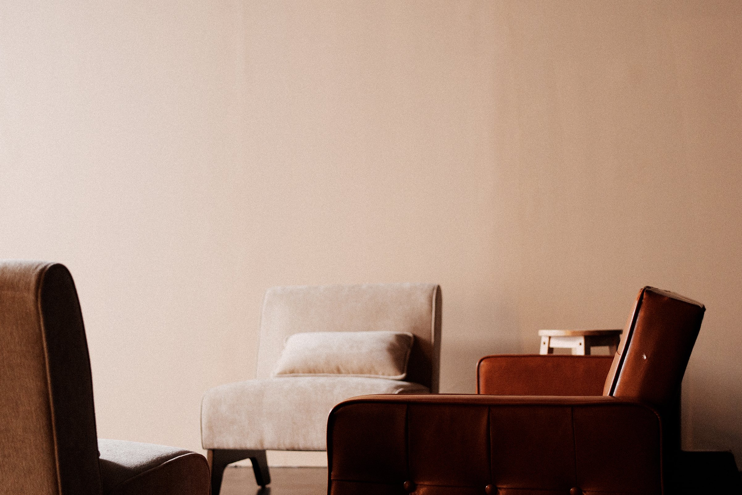 Multiple chairs of different styles and colors are arranged in a room with a plain beige wall.