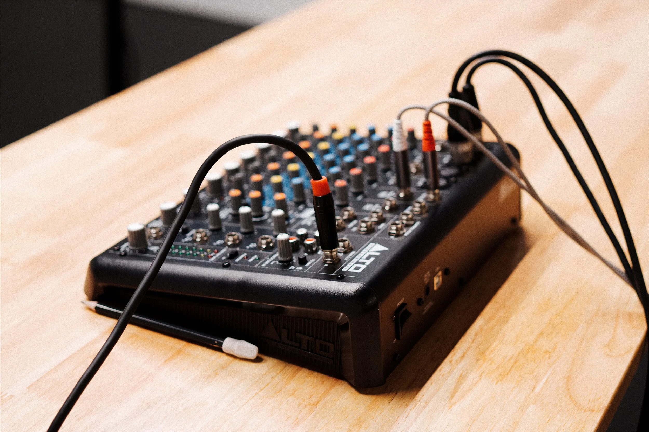 An audio mixer with various knobs and cables is placed on a wooden surface.