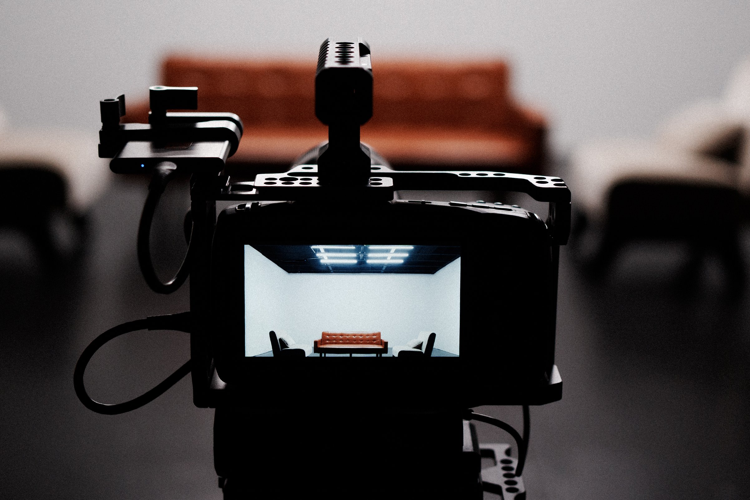 A miniature scene of a living room with a red sofa, small chairs, and a ceiling light, viewed through the lens of a camera or lightbox.