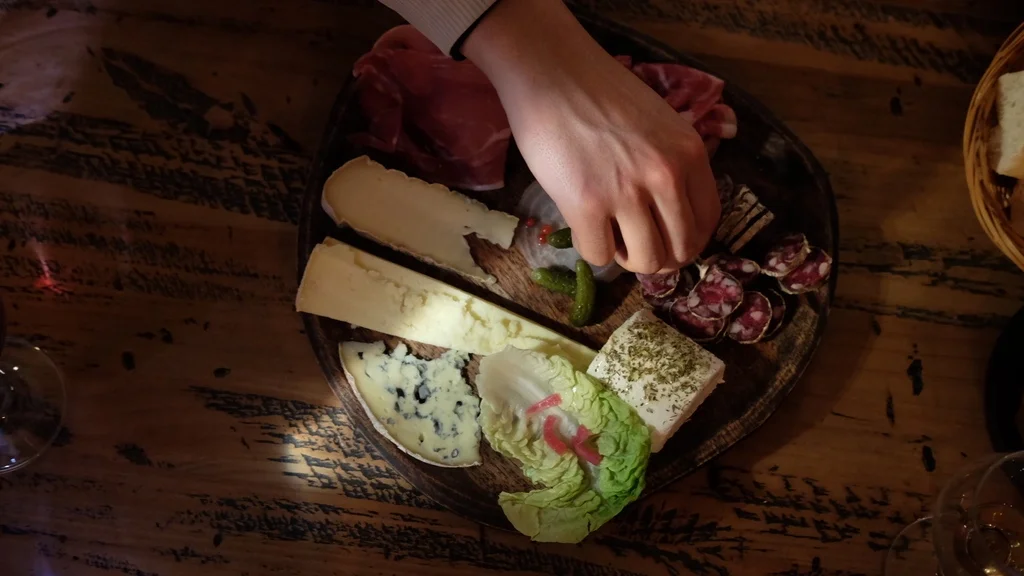 Planches à partager où l'on retrouve du fromage, de la charcuterie et des pickles, une main est par dessus la planche pour se servir