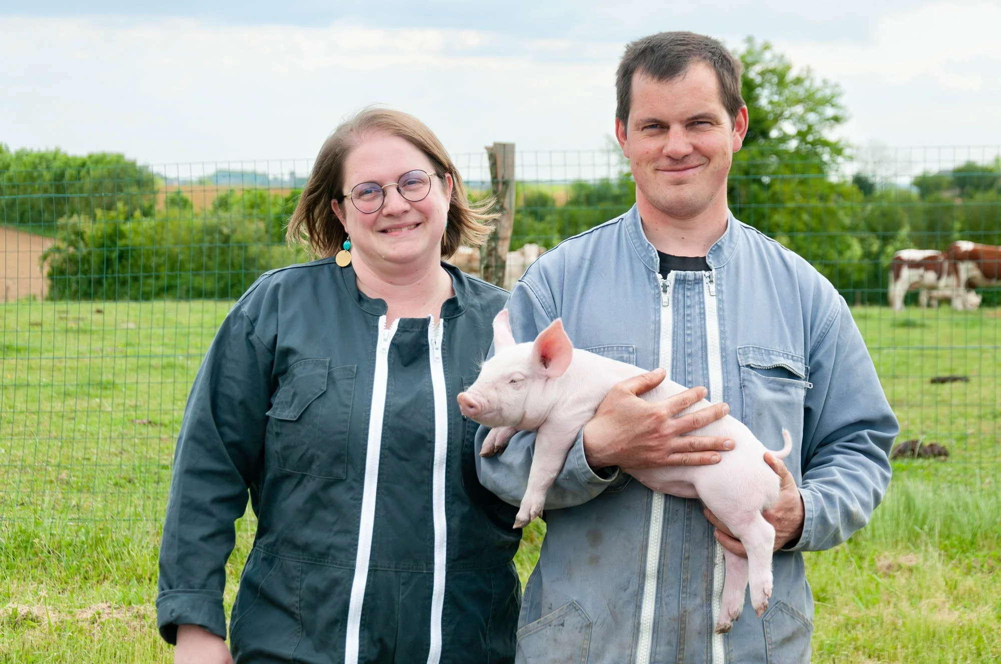 Éleveurs de l’élevage Huart tenant un porcelet dans leur ferme.