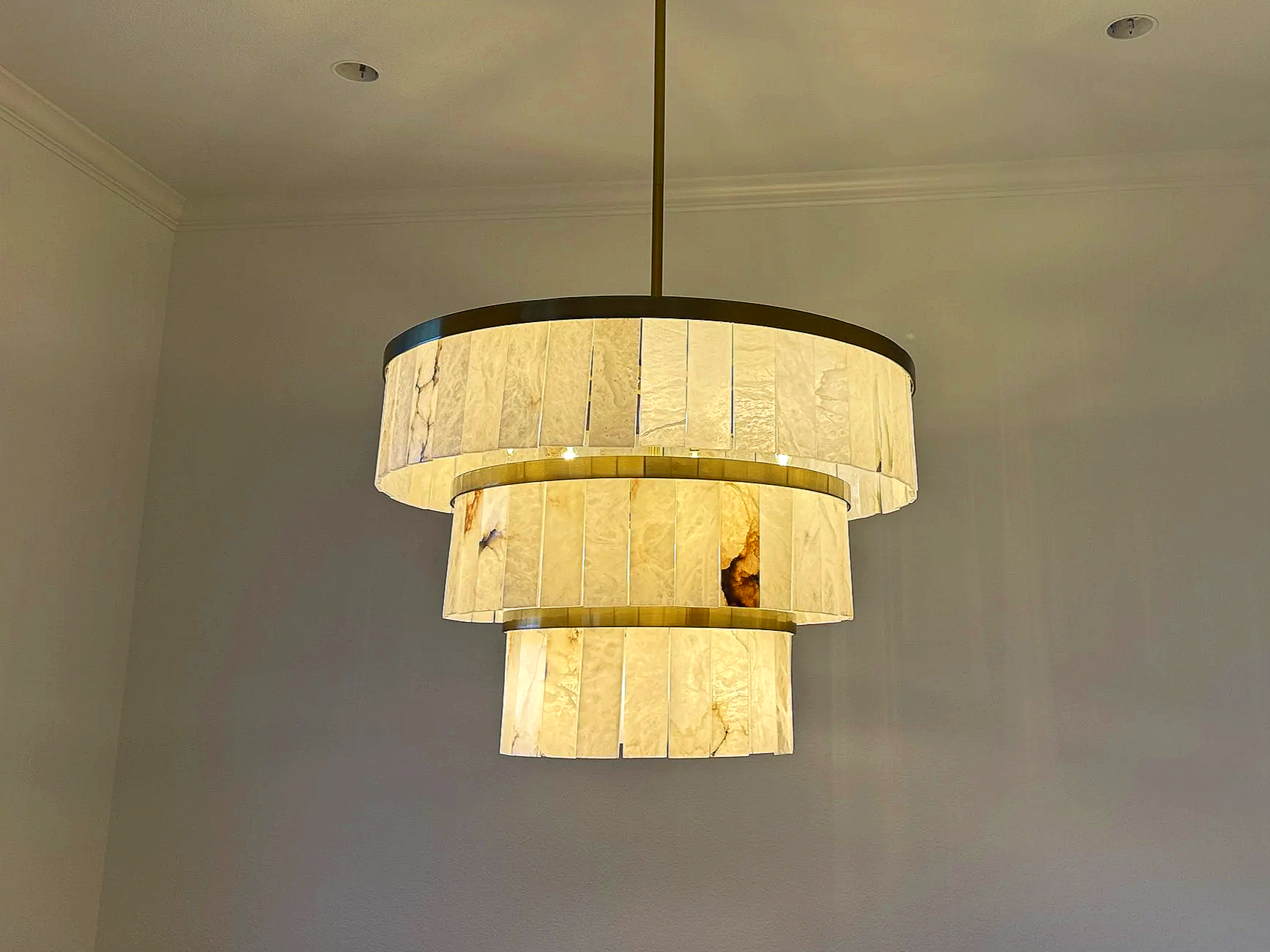 We install all things residential like this modern tiered alabaster chandelier with brass framing, featuring natural stone panels that emit a soft, diffused glow. 
