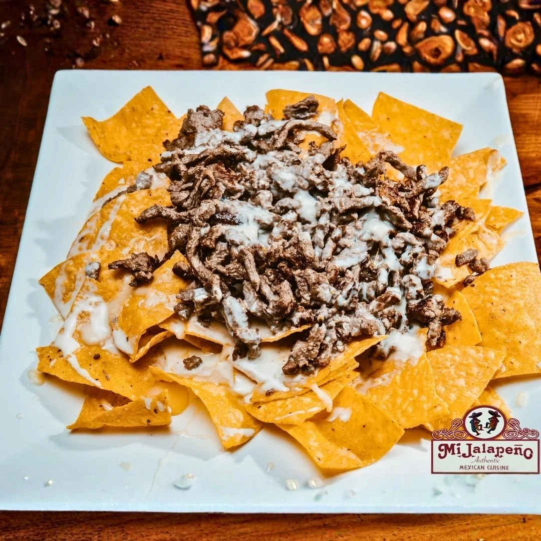 Plate of nachos with melted cheese, shredded beef, and sour cream, served on a white square plate from Mi Jalapeno Mexican Cuisine.