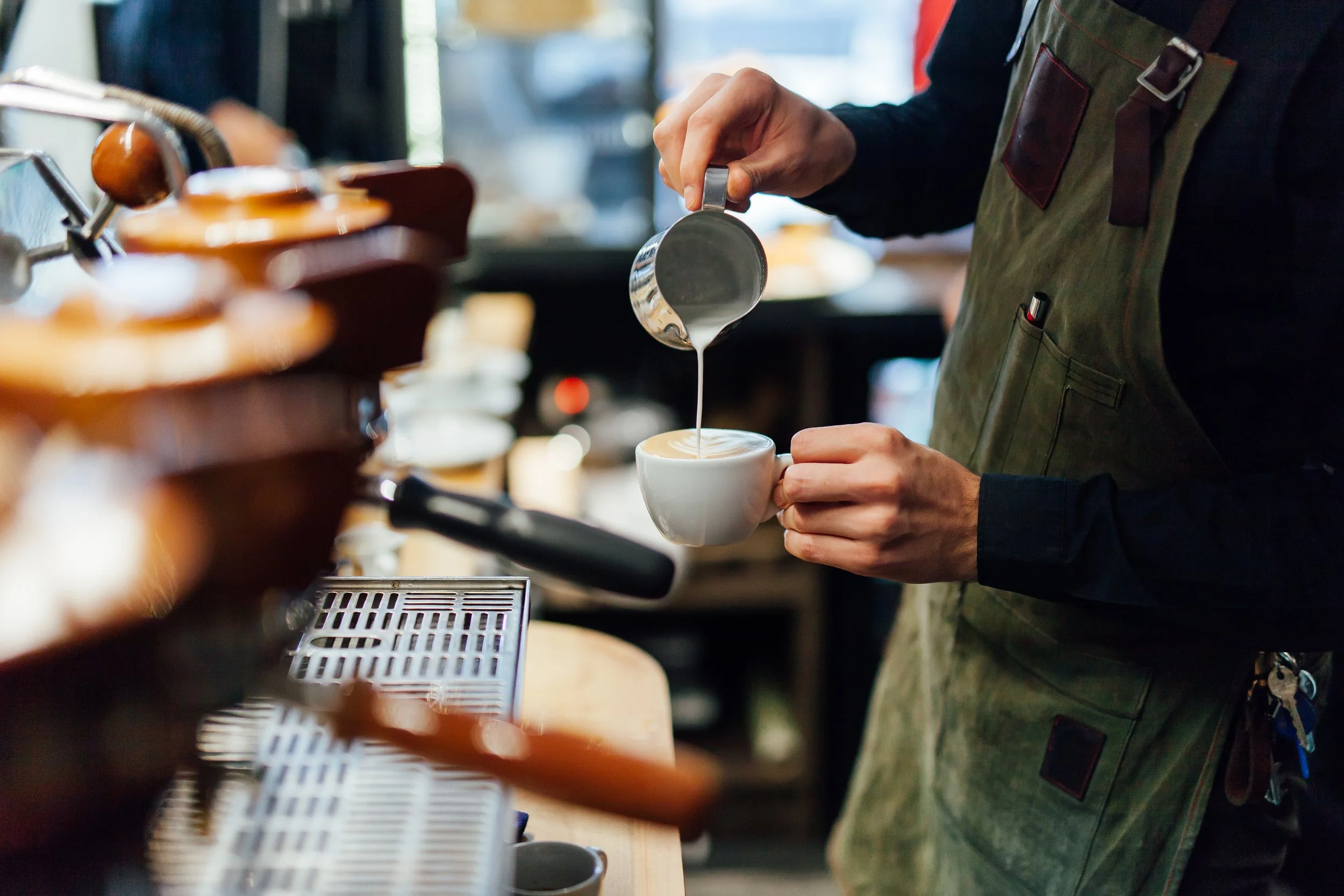 Barista pouring steamed milk into a cup of coffee at a coffee shop.
