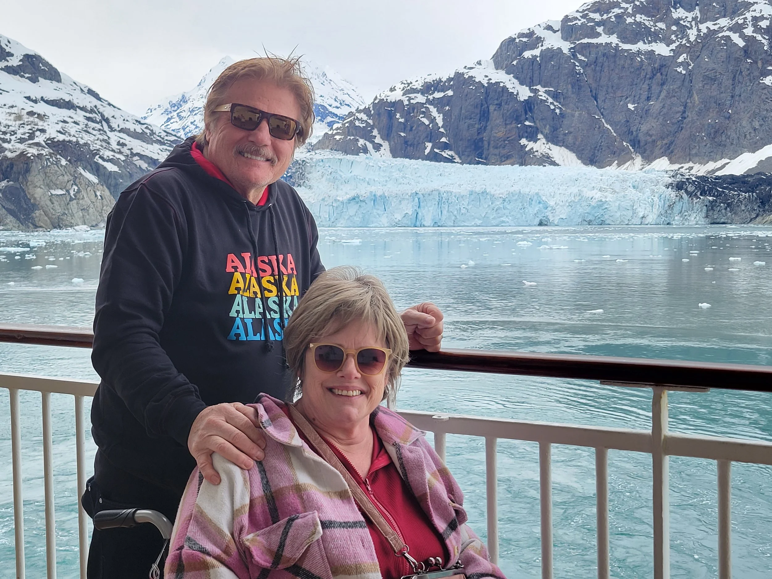 Mitch with Sandy in her wheelchair on the deck of a cruise ship in front of icy terrain