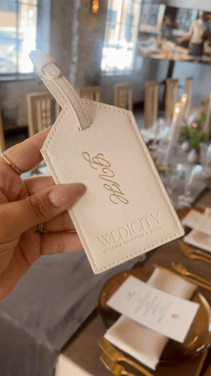 A hand holding a beige luggage tag with custom engraved intials.