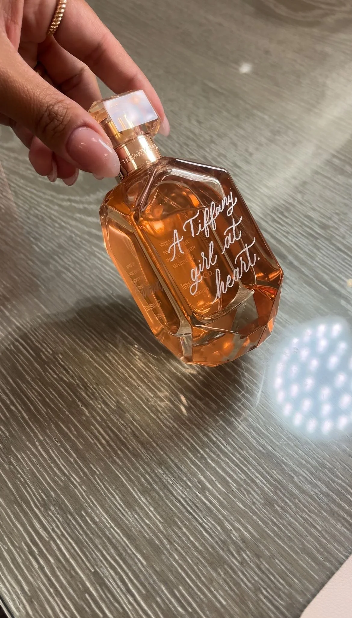 A person's hand holding a Tiffany & Co. perfume bottle with a quote custom engraved, 'A Tiffany girl at heart,' on it.